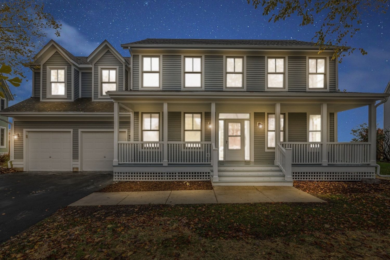 Two-story house at night, lit windows, front porch, garage, siding, and dark sky with stars.