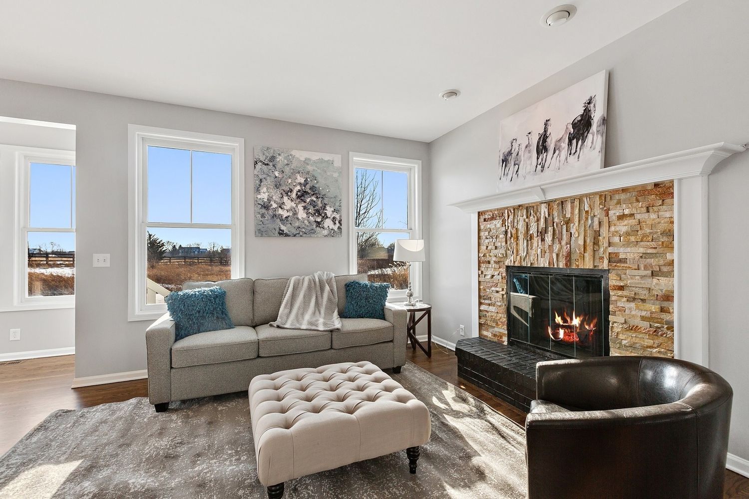 Living room with a fireplace, sofa, windows, and decorative art.