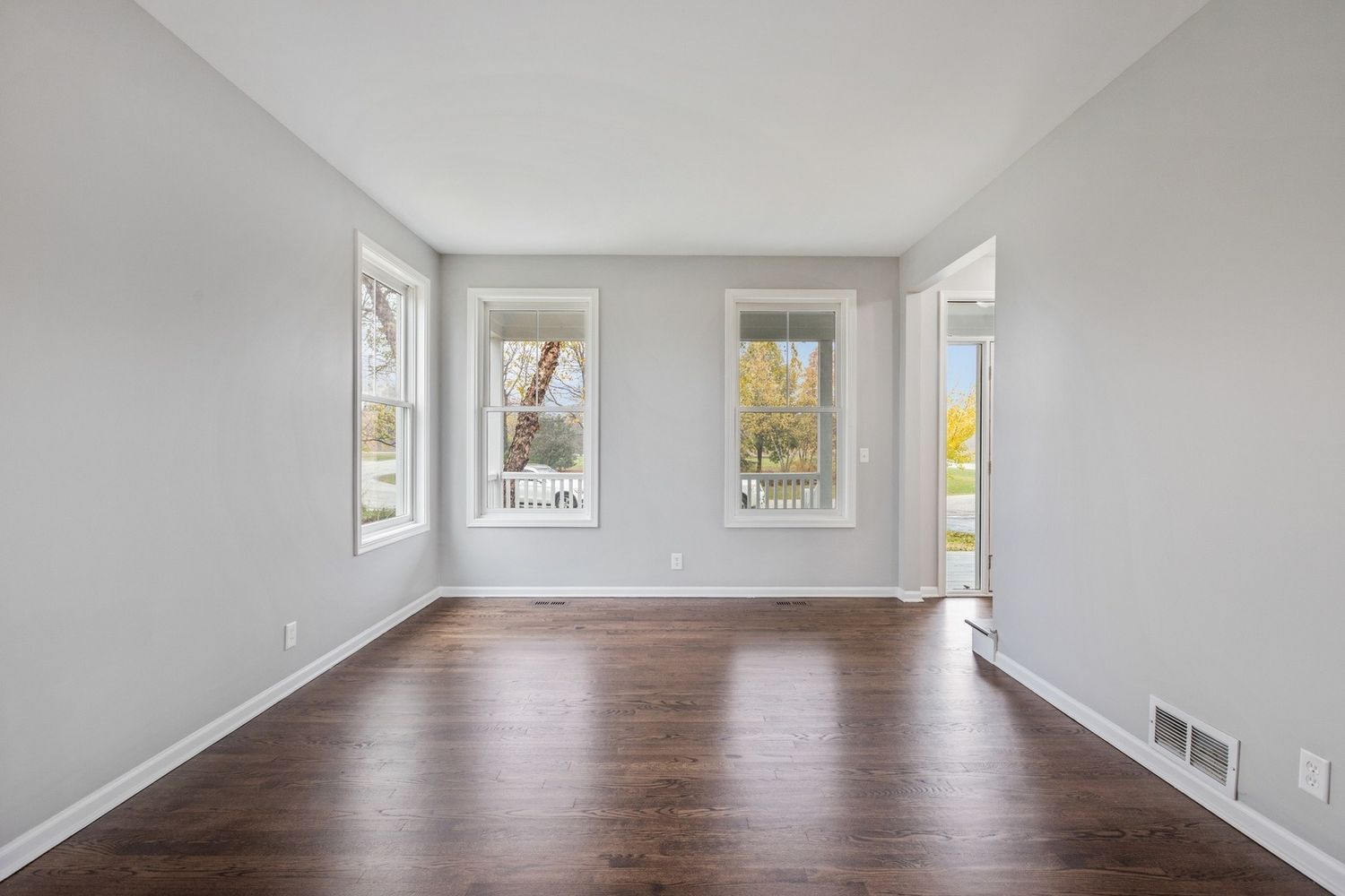 Empty room with gray walls, dark wood floor, two windows, and an open doorway.