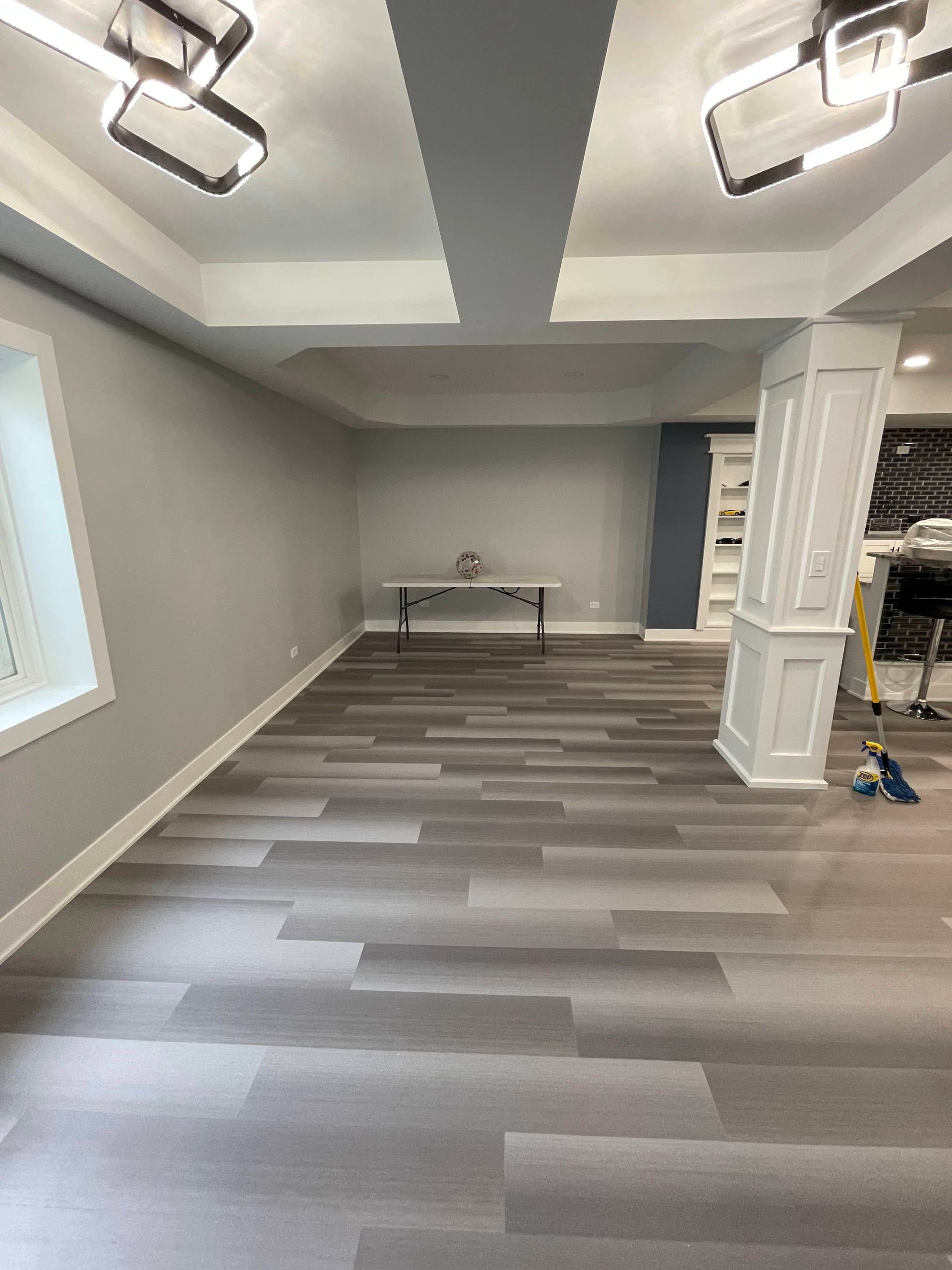 Empty basement room with gray walls, wooden floors, and bright lighting.