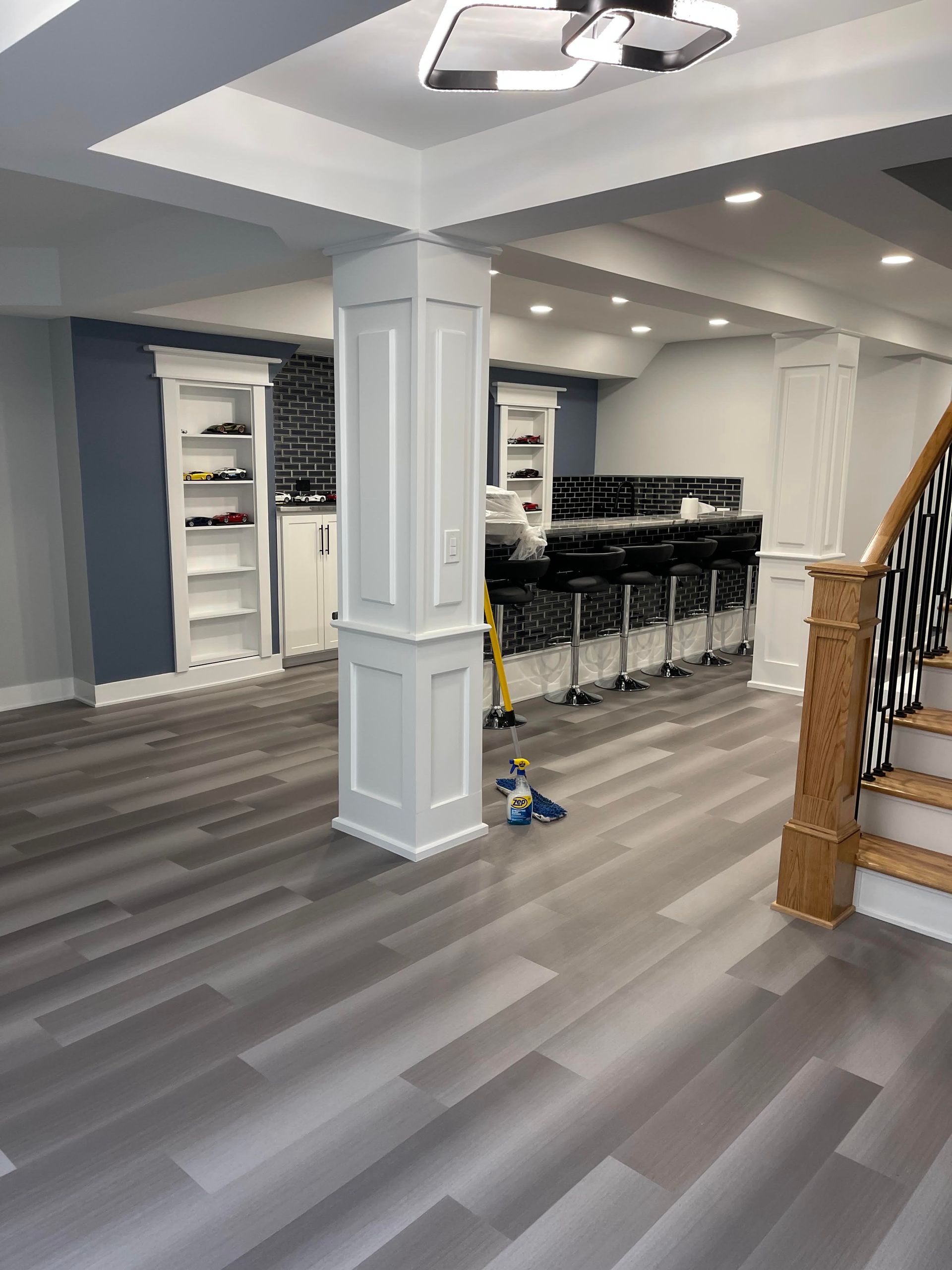 Finished basement with gray flooring, white pillars, bar seating, and built-in cabinets.