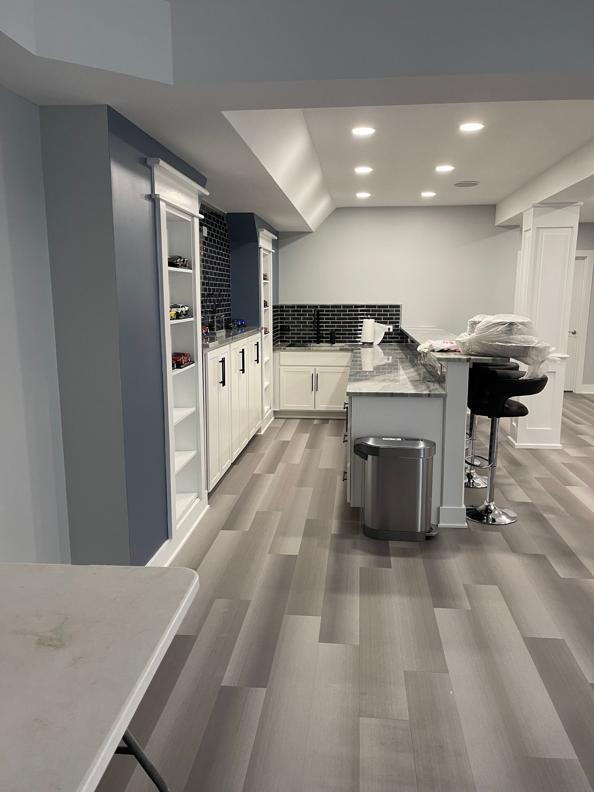 Basement with a bar area, cabinets, countertops, and flooring.  Gray walls, white cabinets, and a stainless steel trash can.