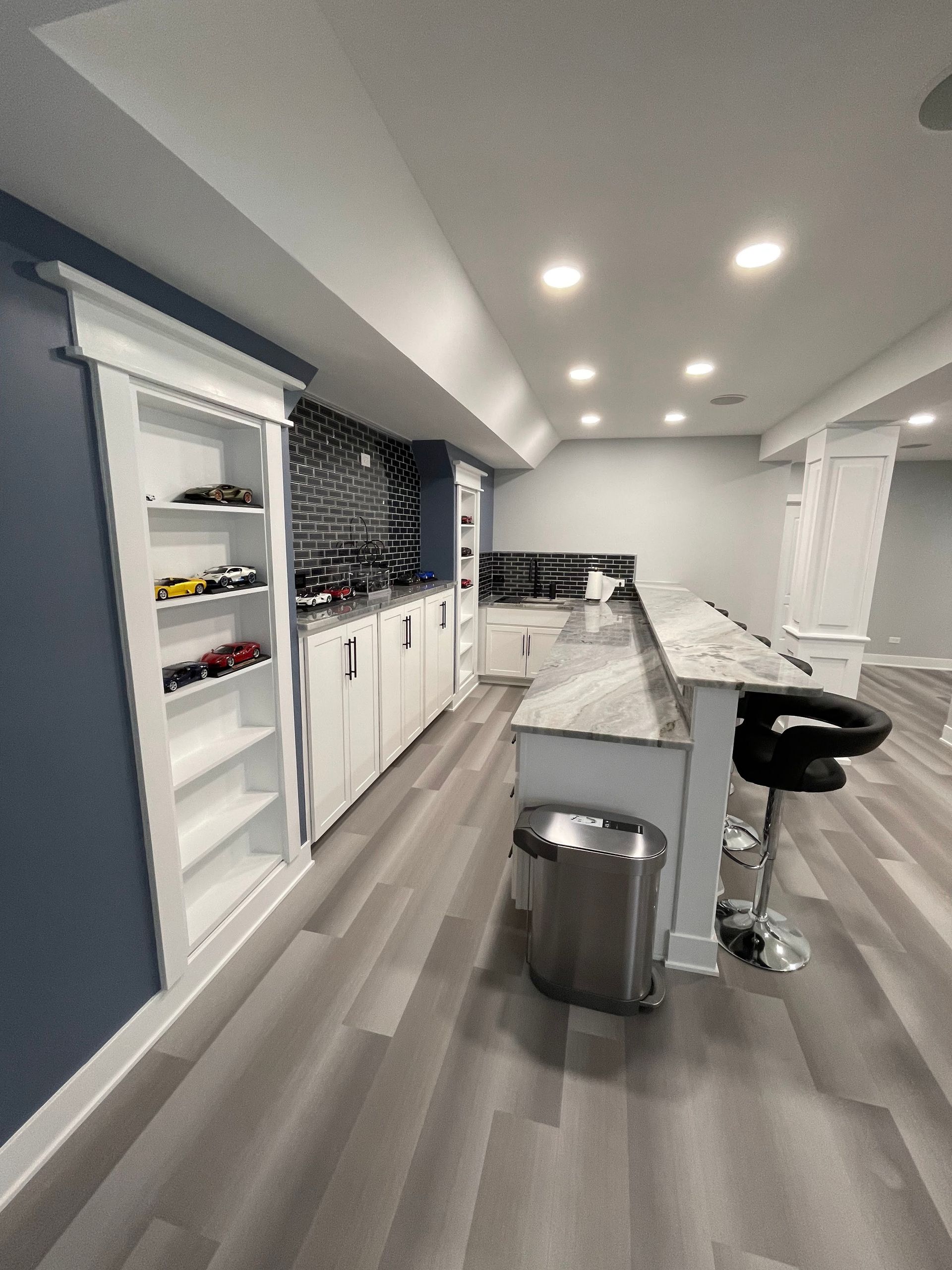 A home bar with white cabinets, granite countertop, and seating.  Blue walls and gray flooring.