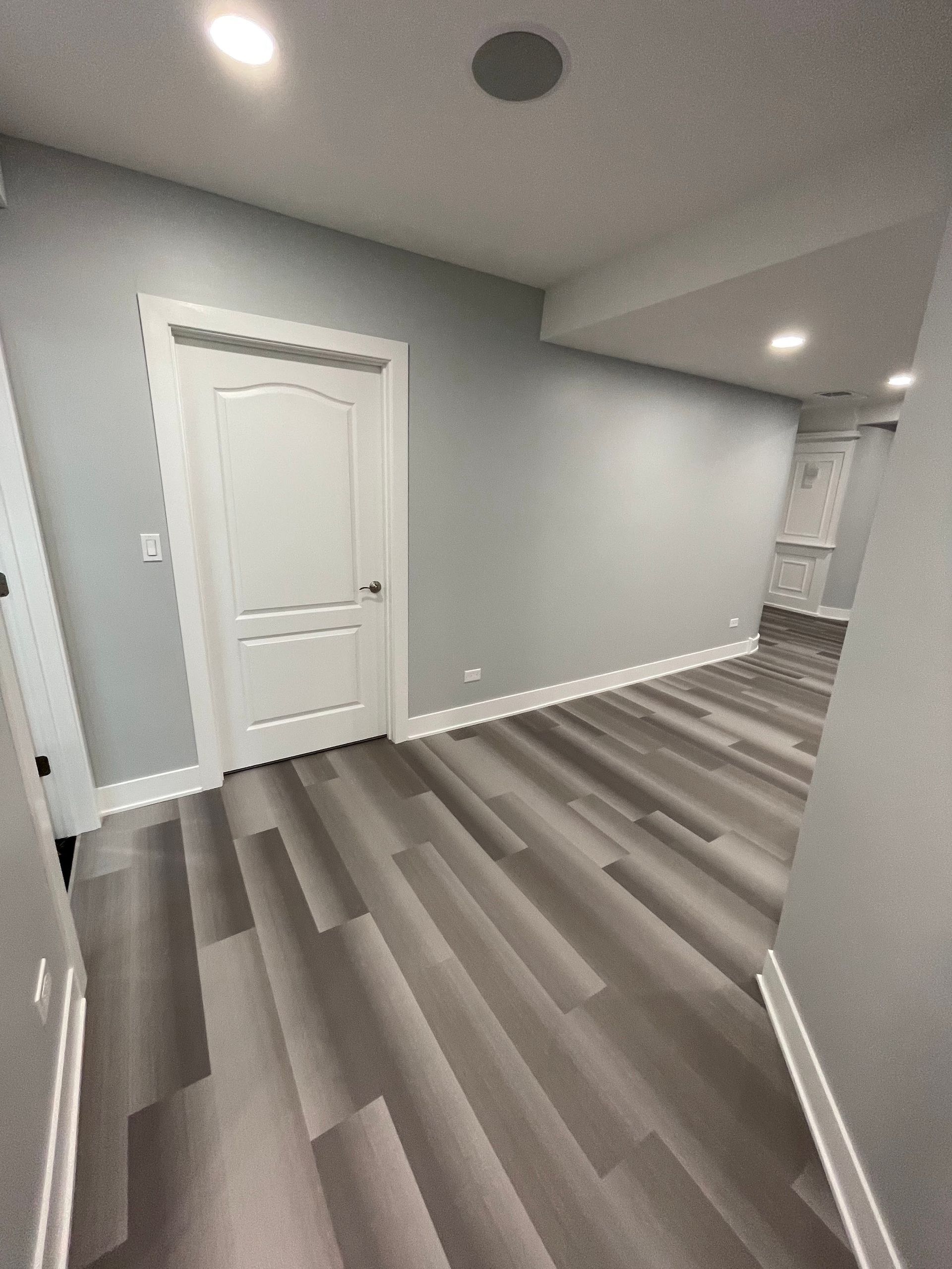 A room with gray walls, white door and trim, and gray-tone wood flooring.