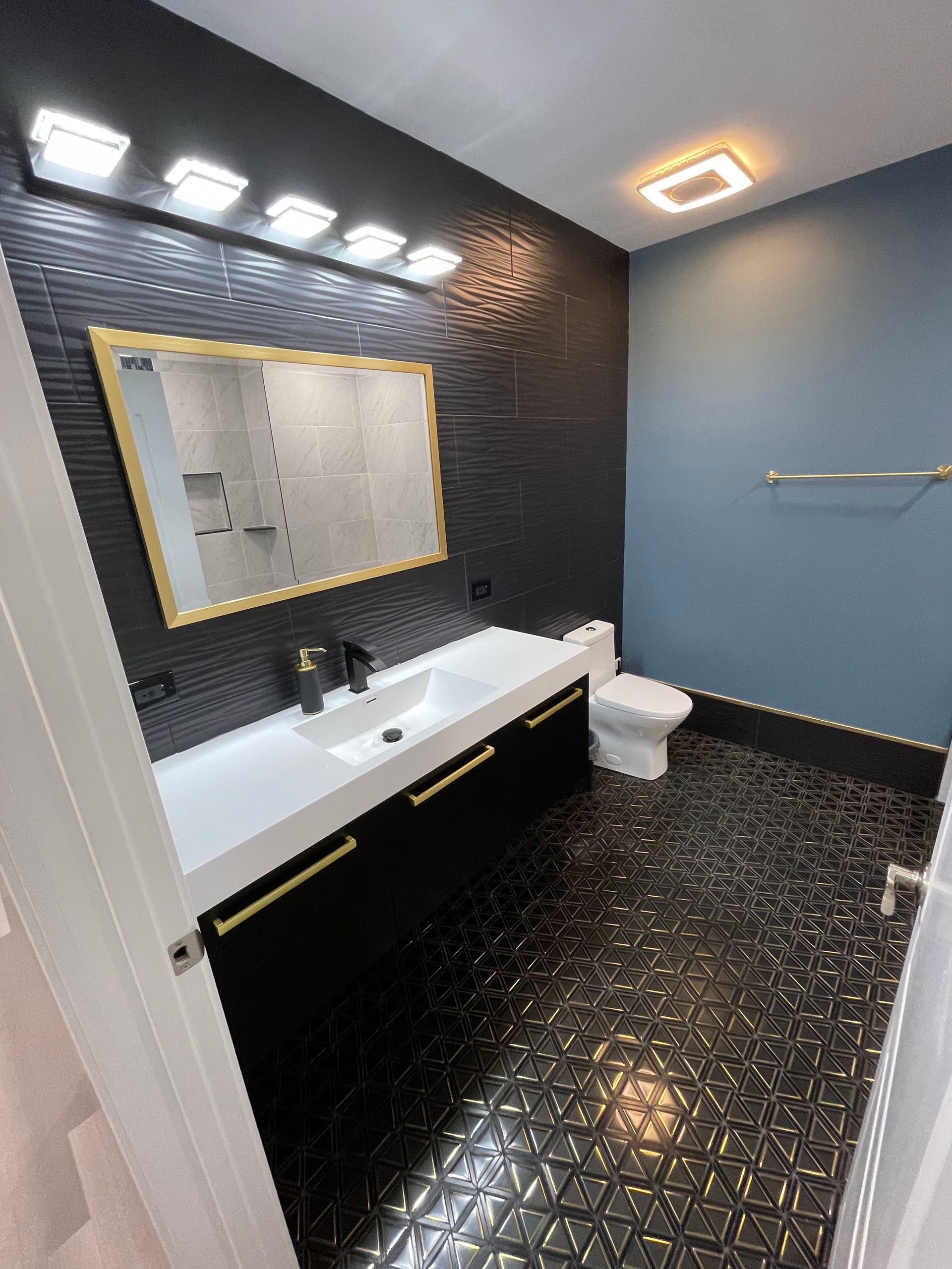 Bathroom with black textured walls, vanity, and floor; gold accents; white sink and toilet; blue wall.