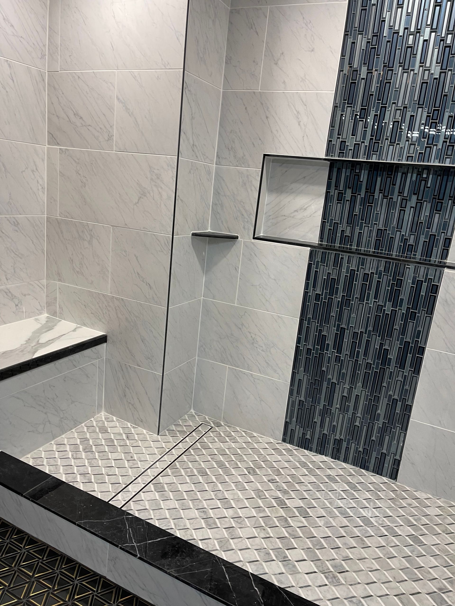 Tiled shower with gray and blue accents, including a built-in bench, a shelf, and a dark border.