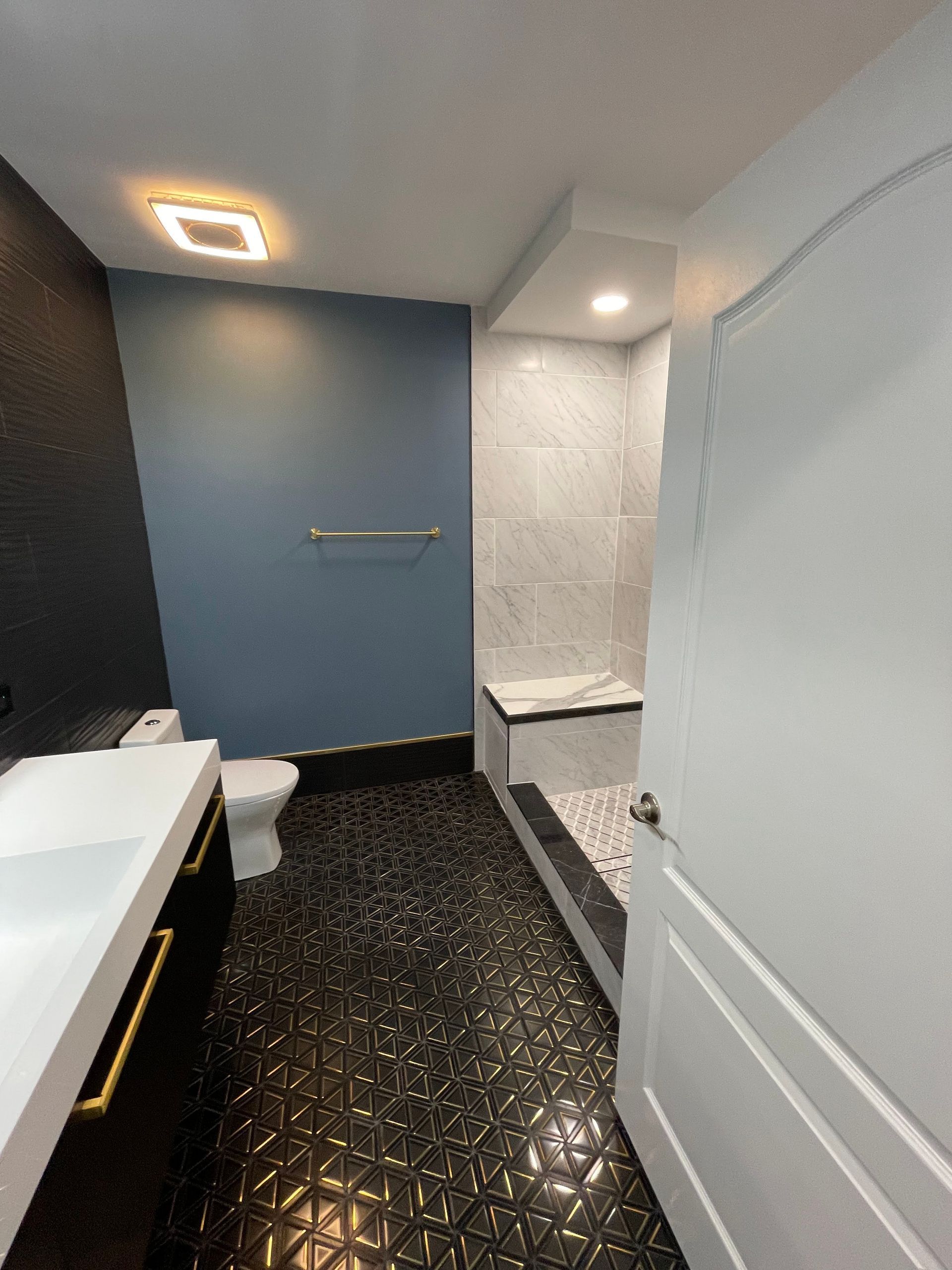 Bathroom with black and gold tiled floor, blue and gray walls, white fixtures, and a shower.