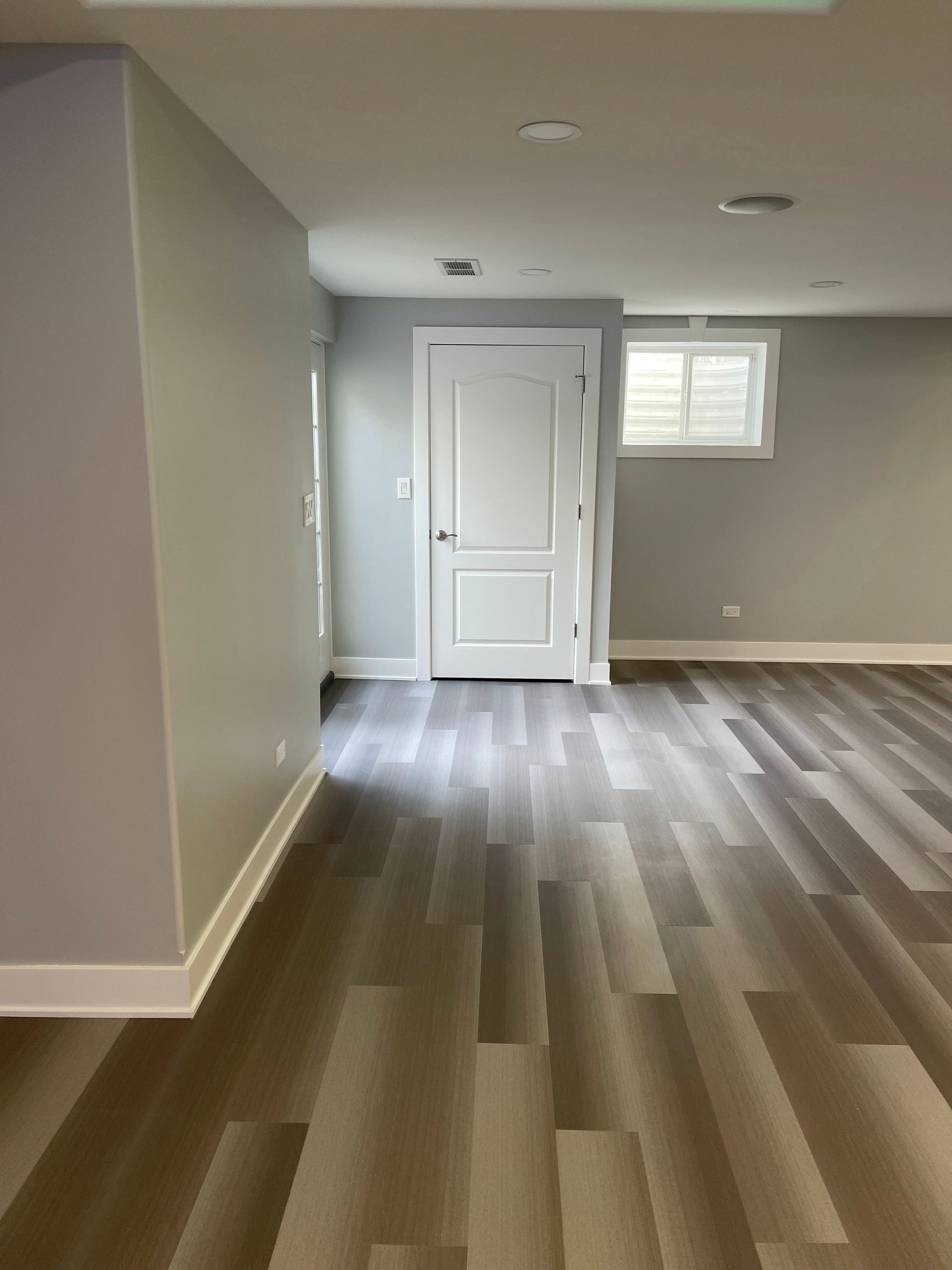 Room with gray walls, white door and trim, and gray wood-look flooring.