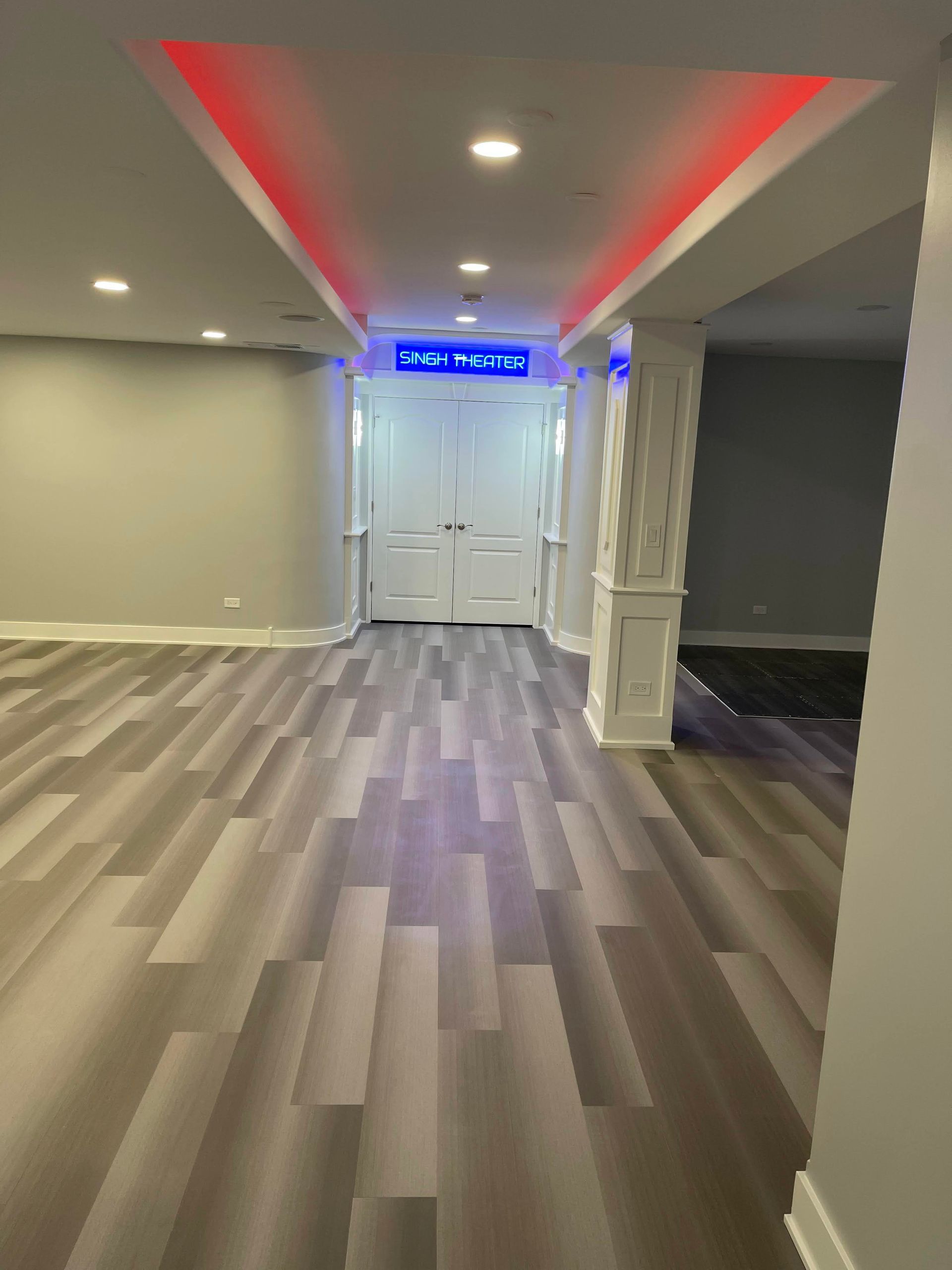 Spacious room with gray wood-look flooring and recessed lighting. White columns and double doors.