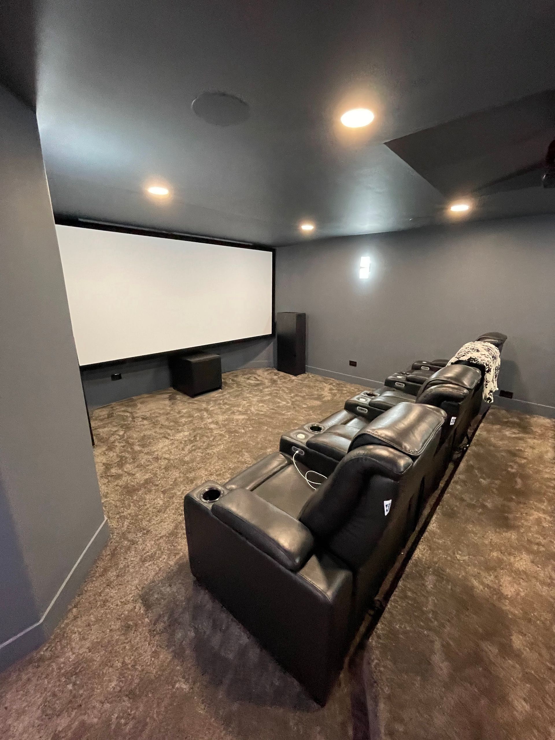 Home theater with gray walls, black leather recliners, screen, speakers, and recessed lighting.