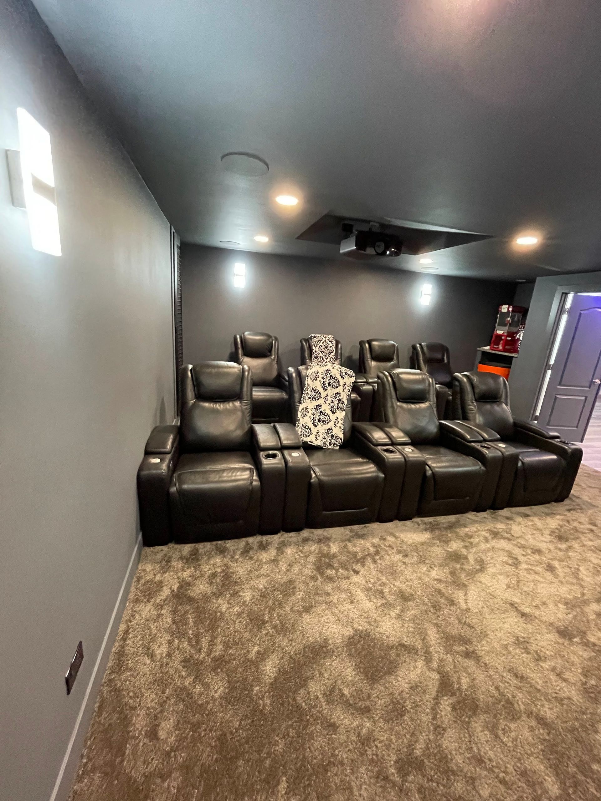 Home theater with black reclining seats, projector, gray walls, and beige carpet.
