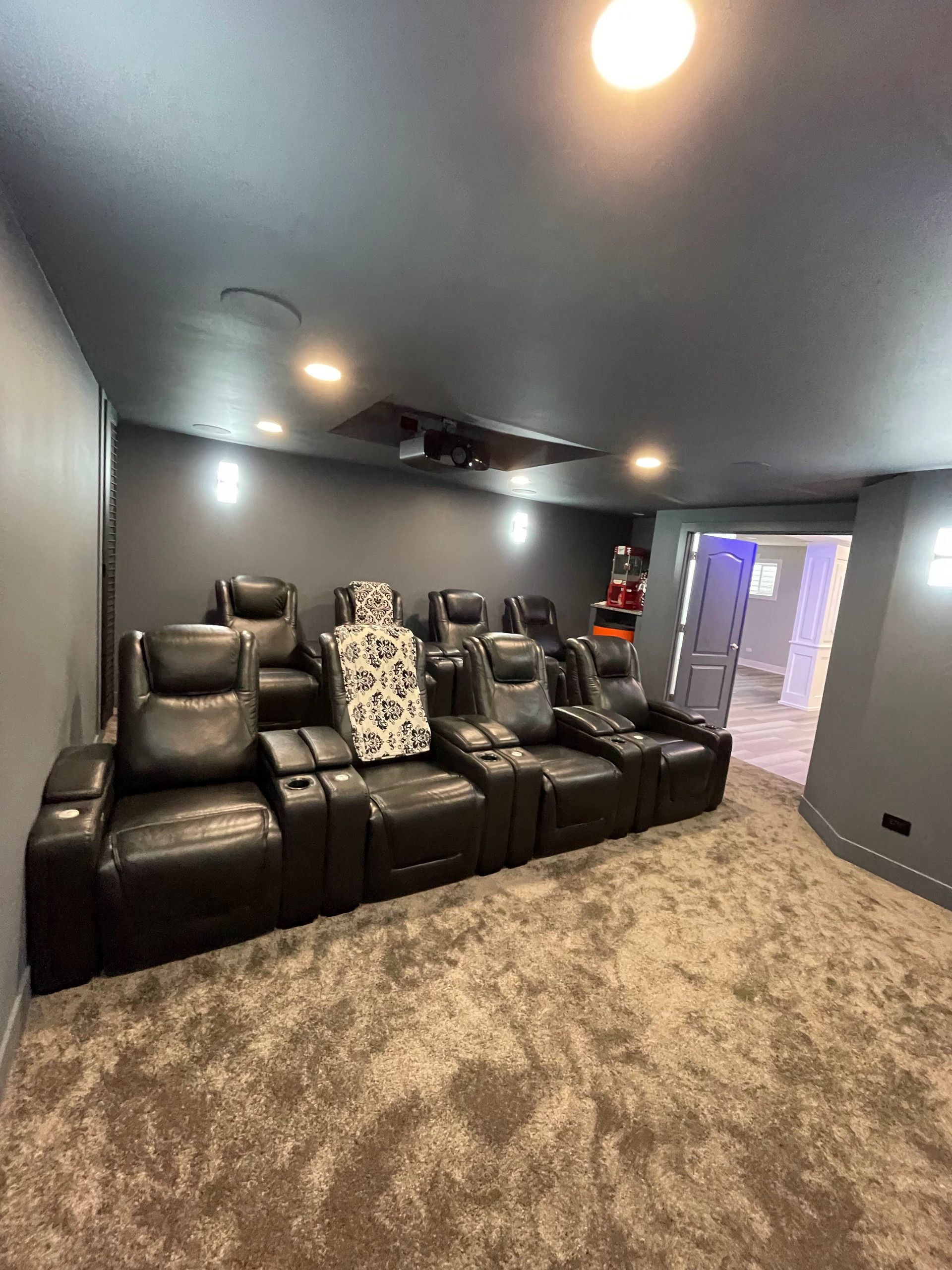 Home theater with black leather reclining seats, gray walls, and plush carpet.