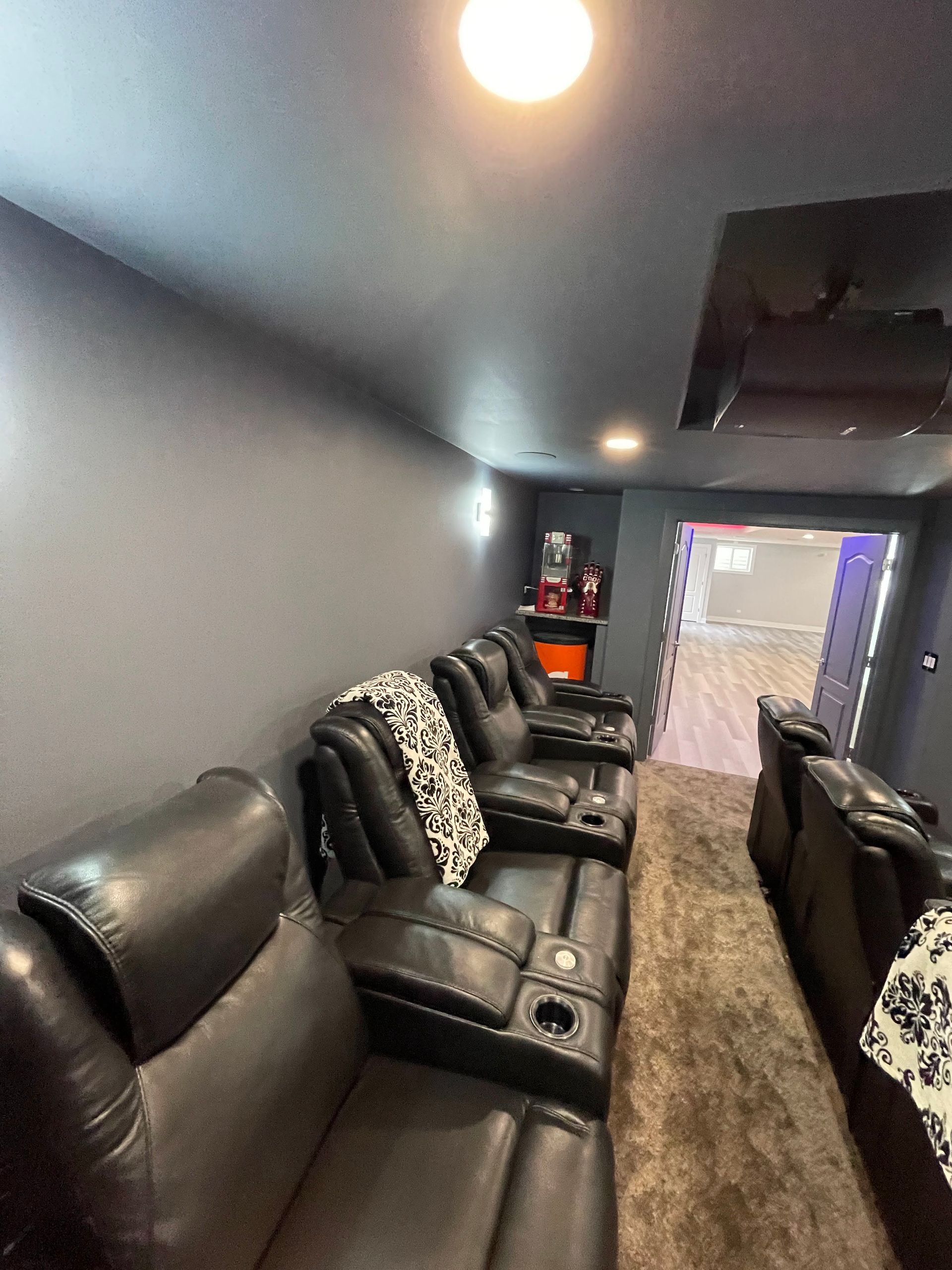 Home theater with black reclining chairs, gray walls, and carpet; door in the background.