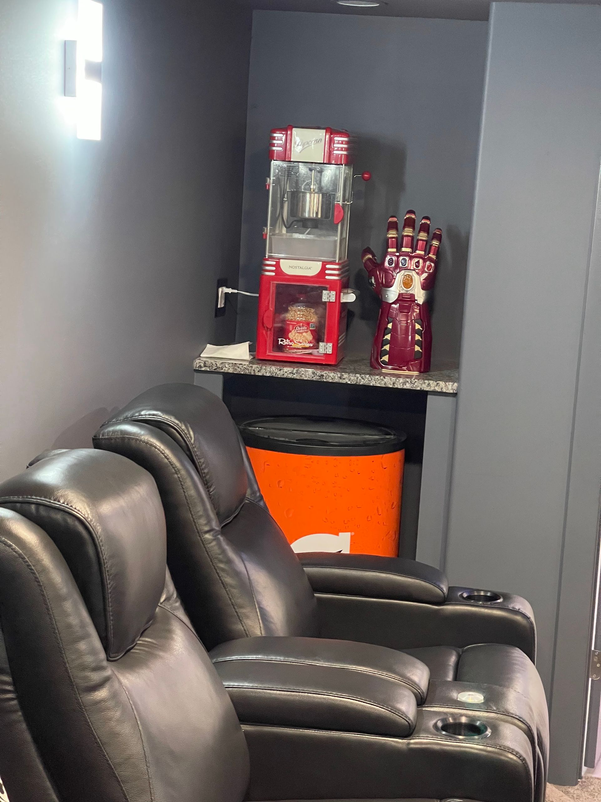 Two black leather recliners sit under a built-in shelf with a popcorn machine and a red Infinity Gauntlet.
