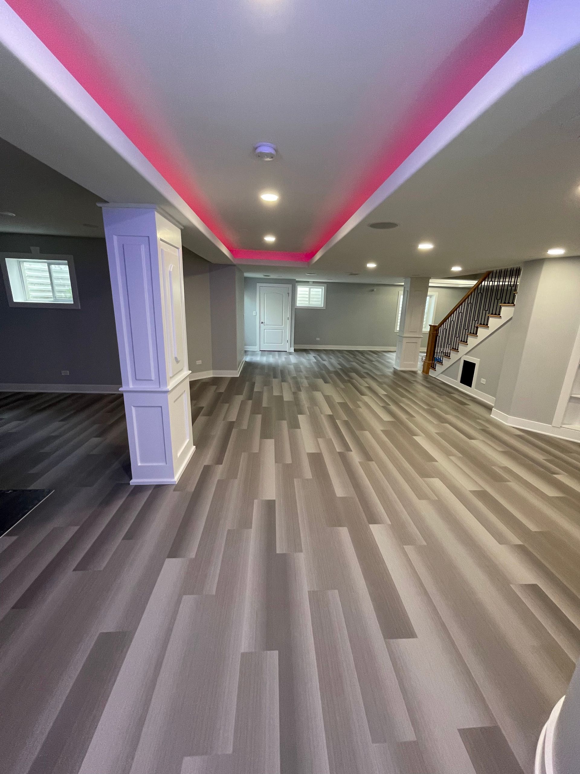 Spacious basement with gray wood-look flooring, white trim, recessed lighting, and pink overhead accent lights.