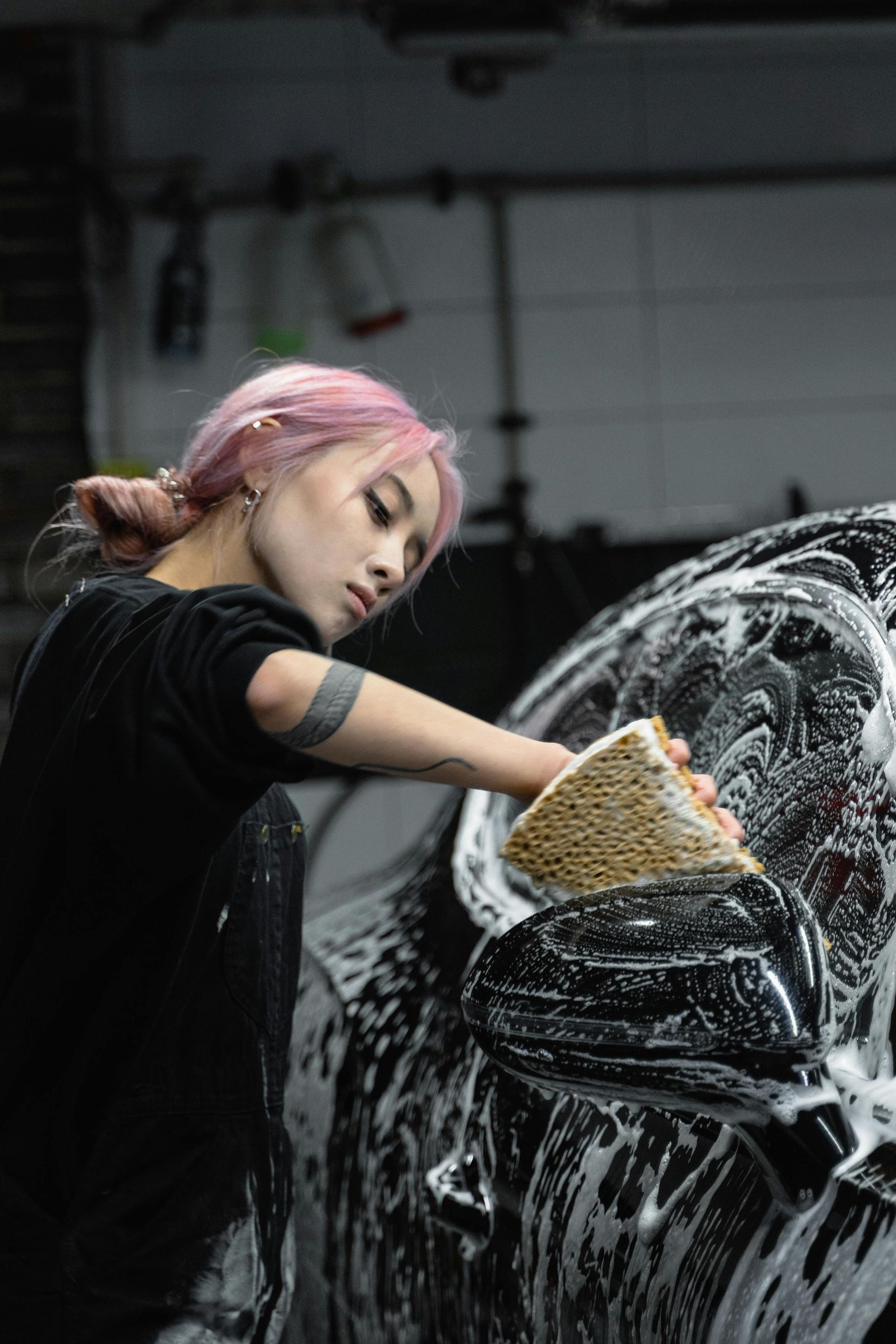 A woman is washing a car with a sponge.