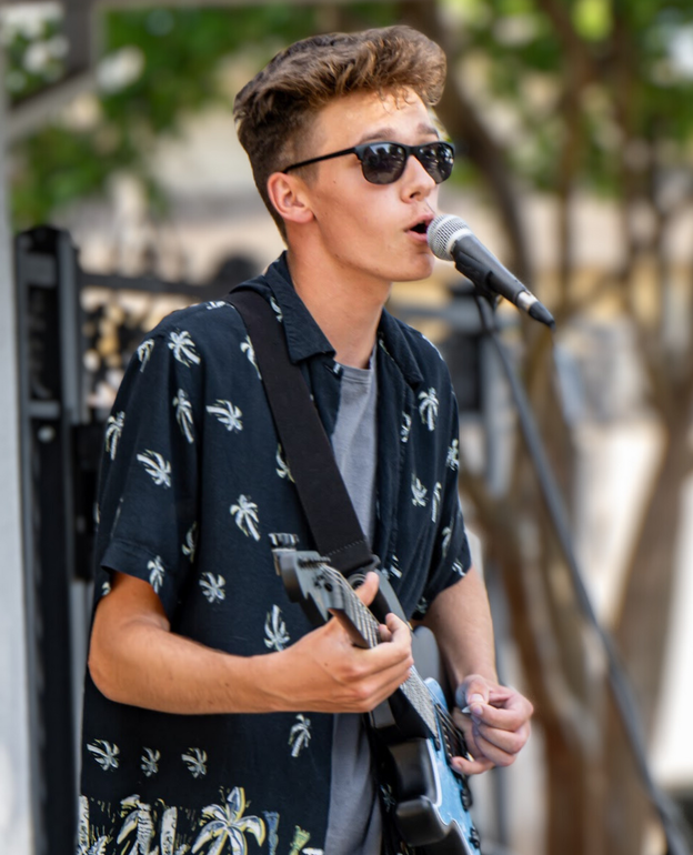 A young man is singing into a microphone while holding a guitar.