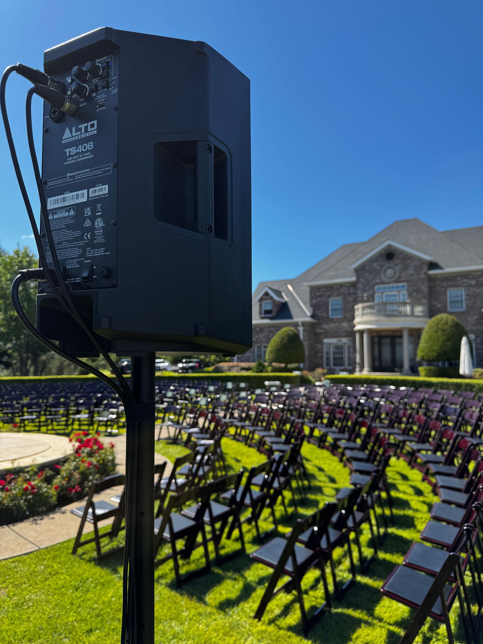 Outdoor graduation setup with rows of black chairs on green lawn and a large speaker in front of a stone building