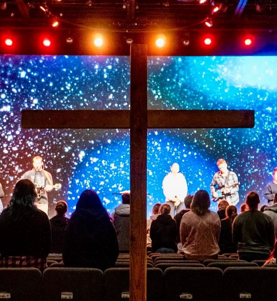 A group of people are sitting in front of a large screen with a cross in the middle.
