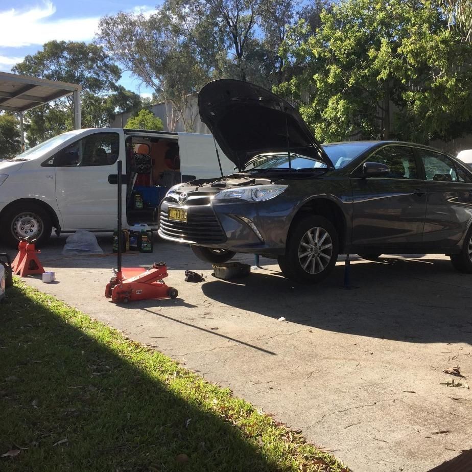 A Car With The Hood Up Is Being Worked On In A Driveway — SG Mobile Mechanic In Lake Macquarie, NSW