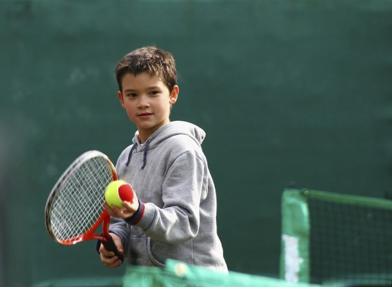 Young tennis player in a gray hoodie holding a racket and ball on a court