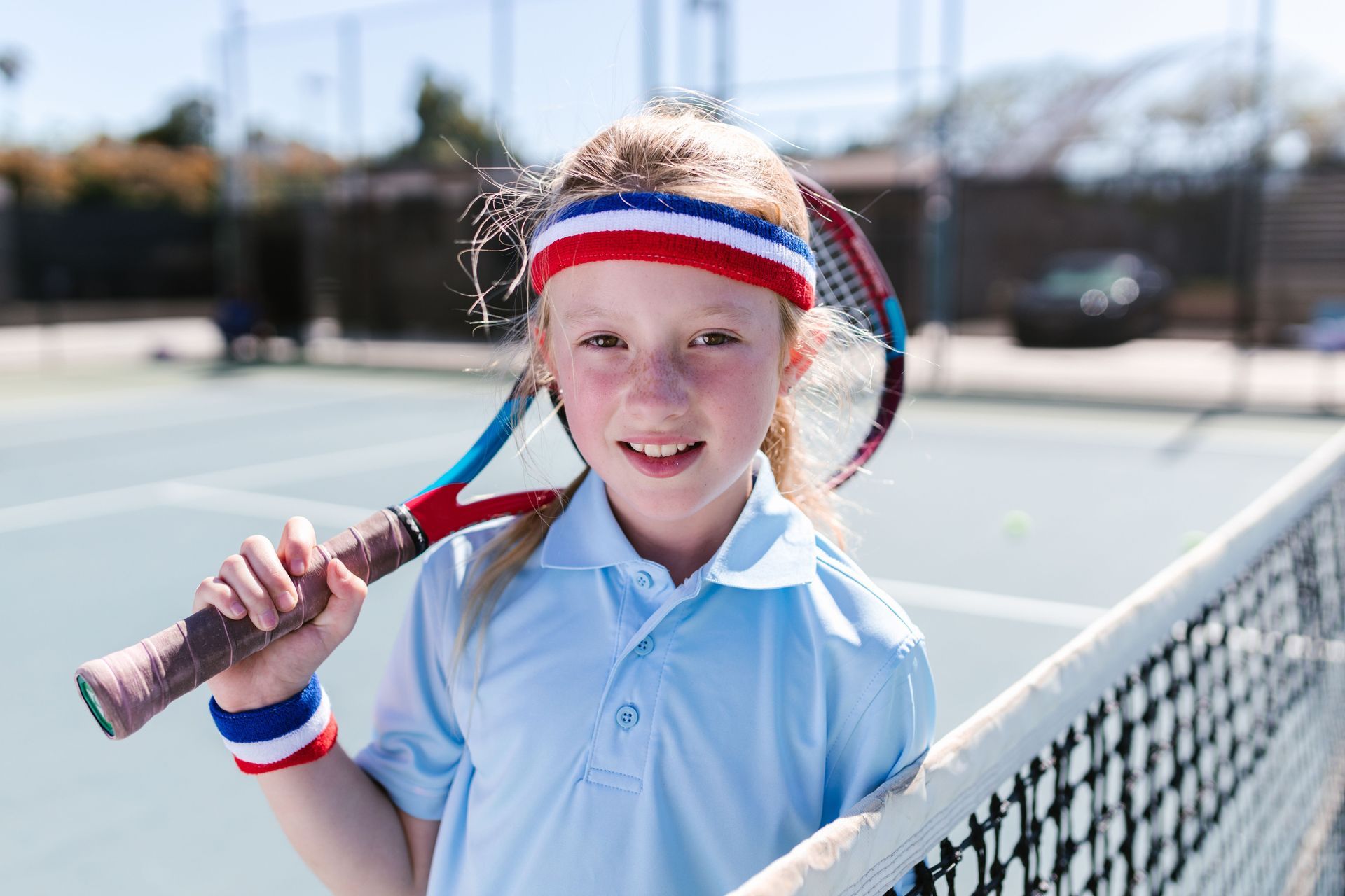 Smiling tennis player in a blue shirt and headband holding a racket on an outdoor court