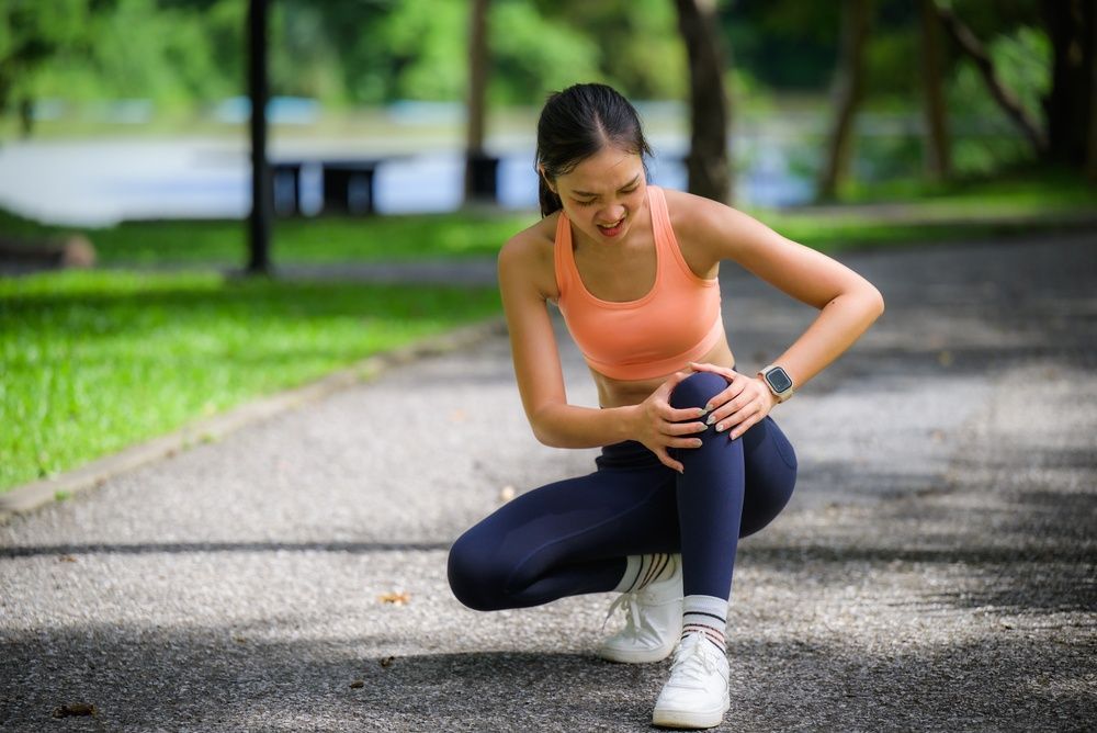 Woman kneeling on a park path, holding her knee after a run.