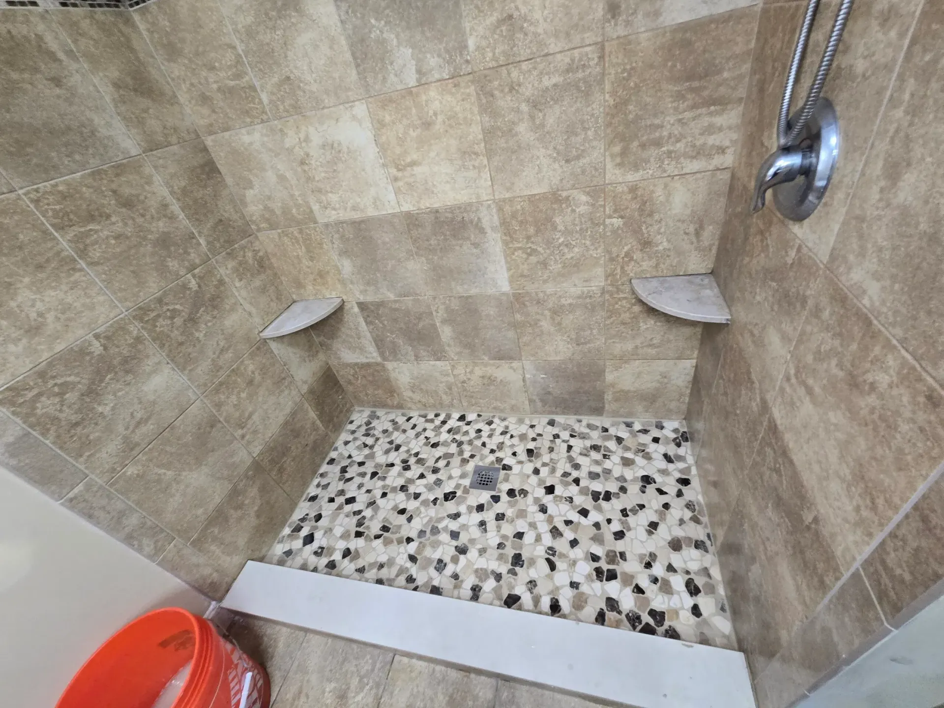 A walk in shower with a tiled floor and a shower head.