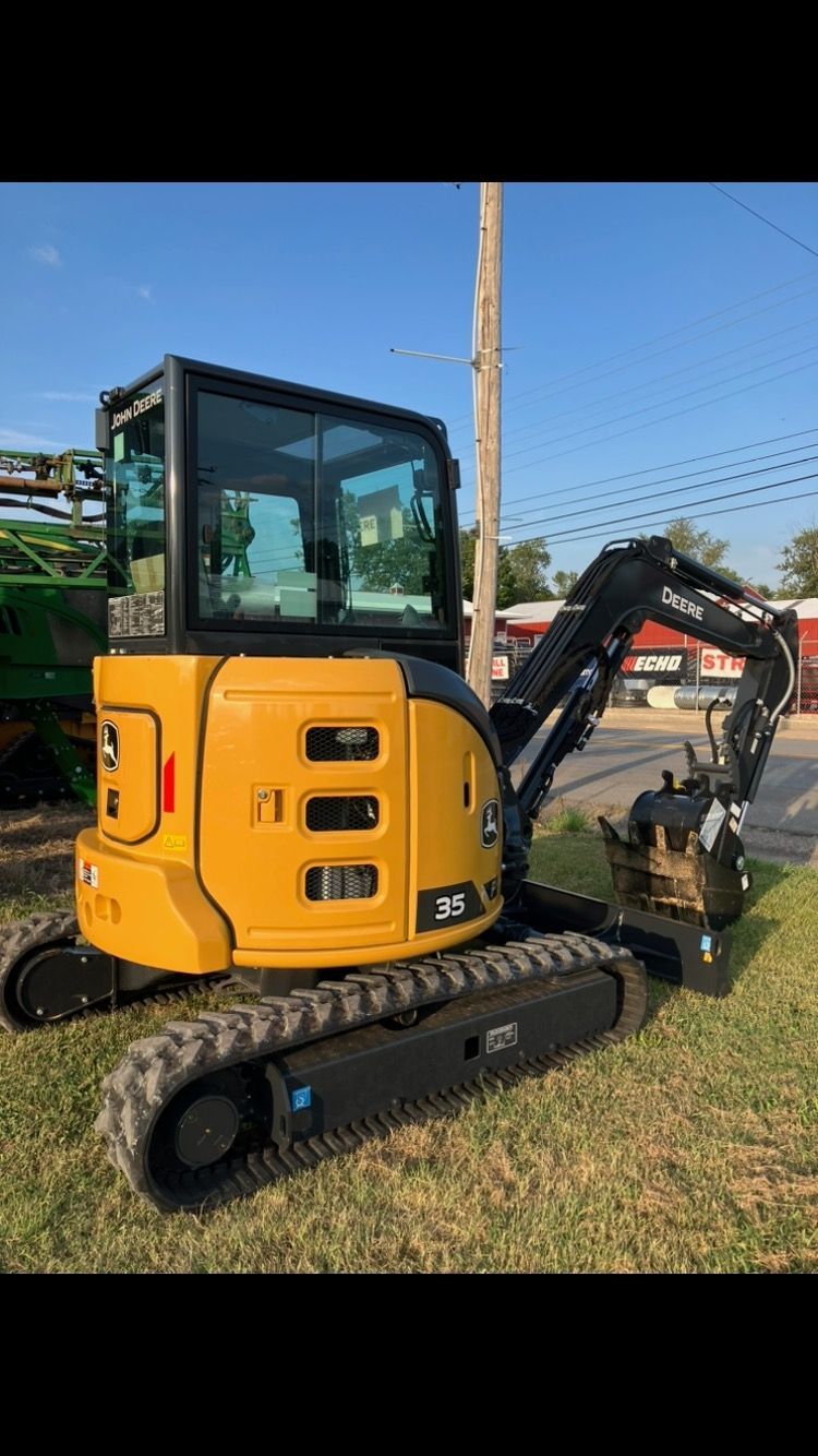 A small yellow excavator is parked in the grass next to a pole.