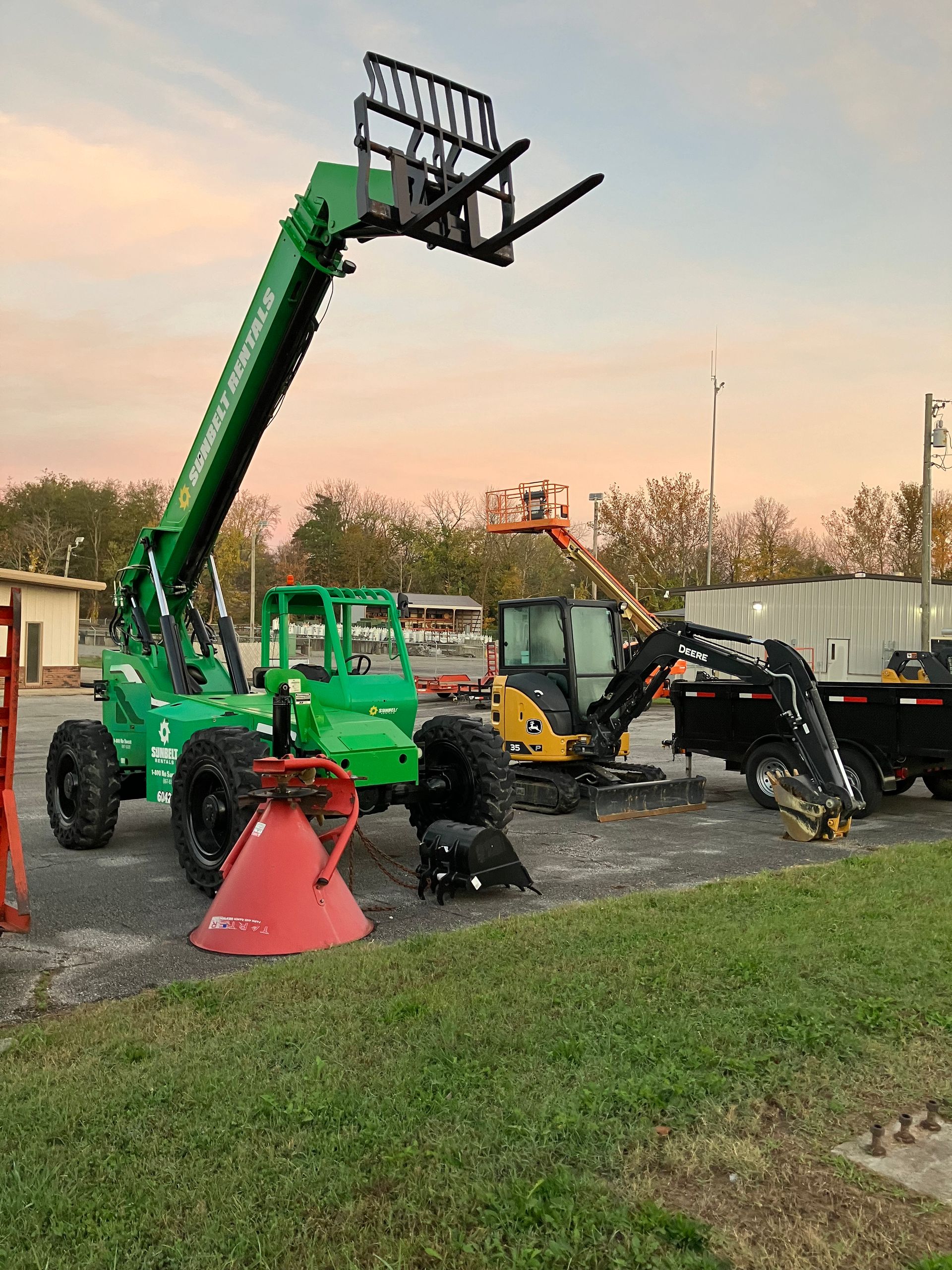 A green forklift is parked in a parking lot next to a truck.
