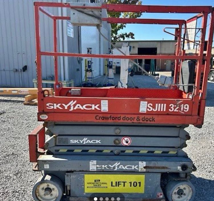 A skyjack scissor lift is parked in front of a building