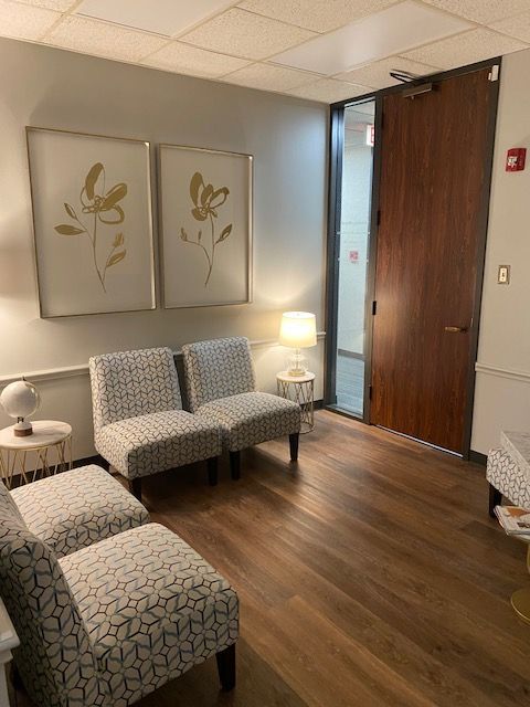 A waiting room with chairs , a table , a lamp and a door.