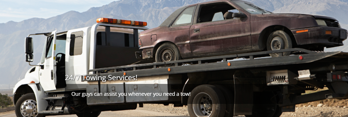 Tow truck hauling a damaged brown sedan on a flatbed in a desert setting