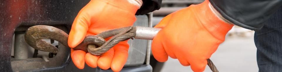 Orange-gloved hands holding a metal tool near a wheel assembly on a vehicle or machine