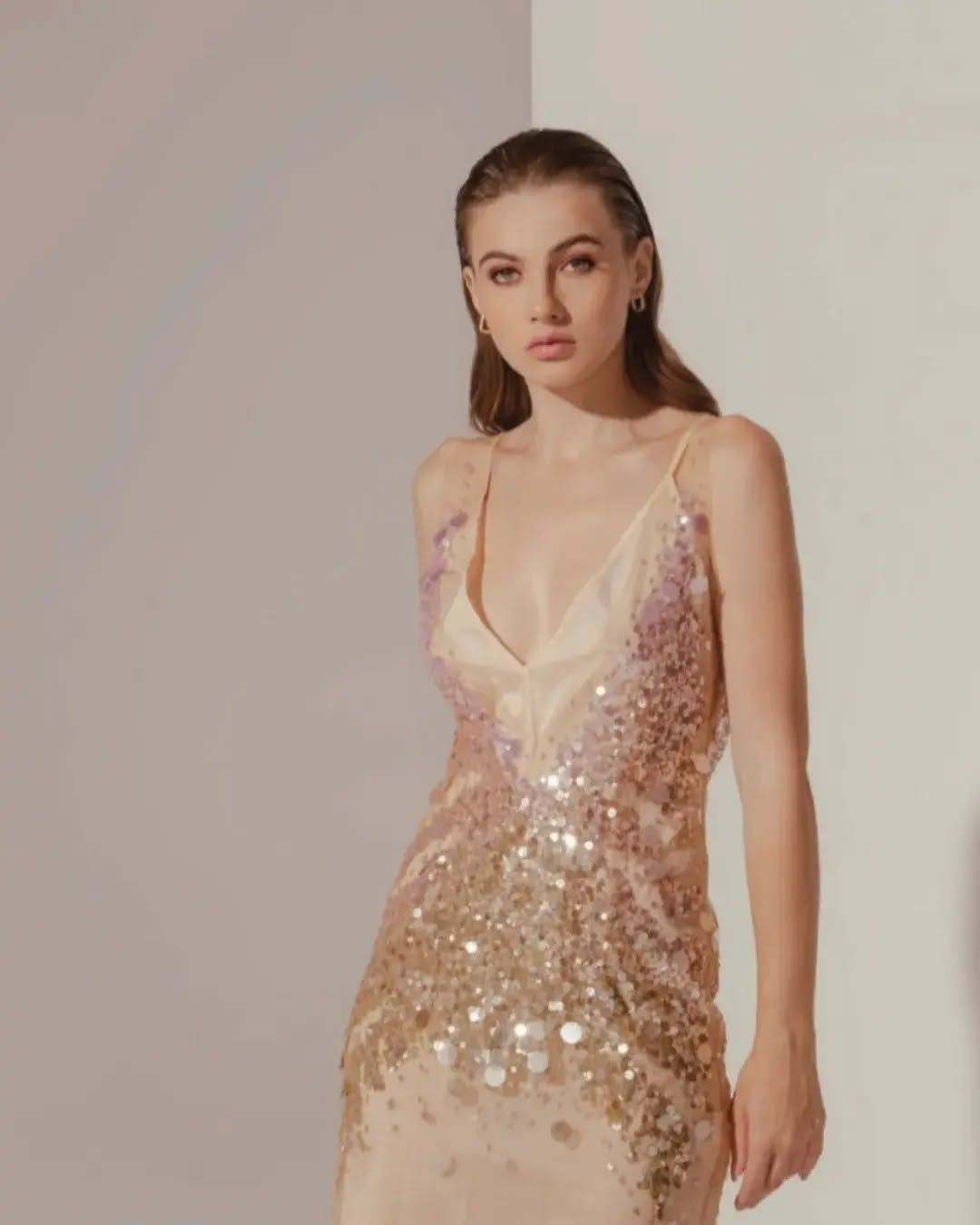 Una donna indossa un abito con paillettes ed è in piedi accanto a un muro.