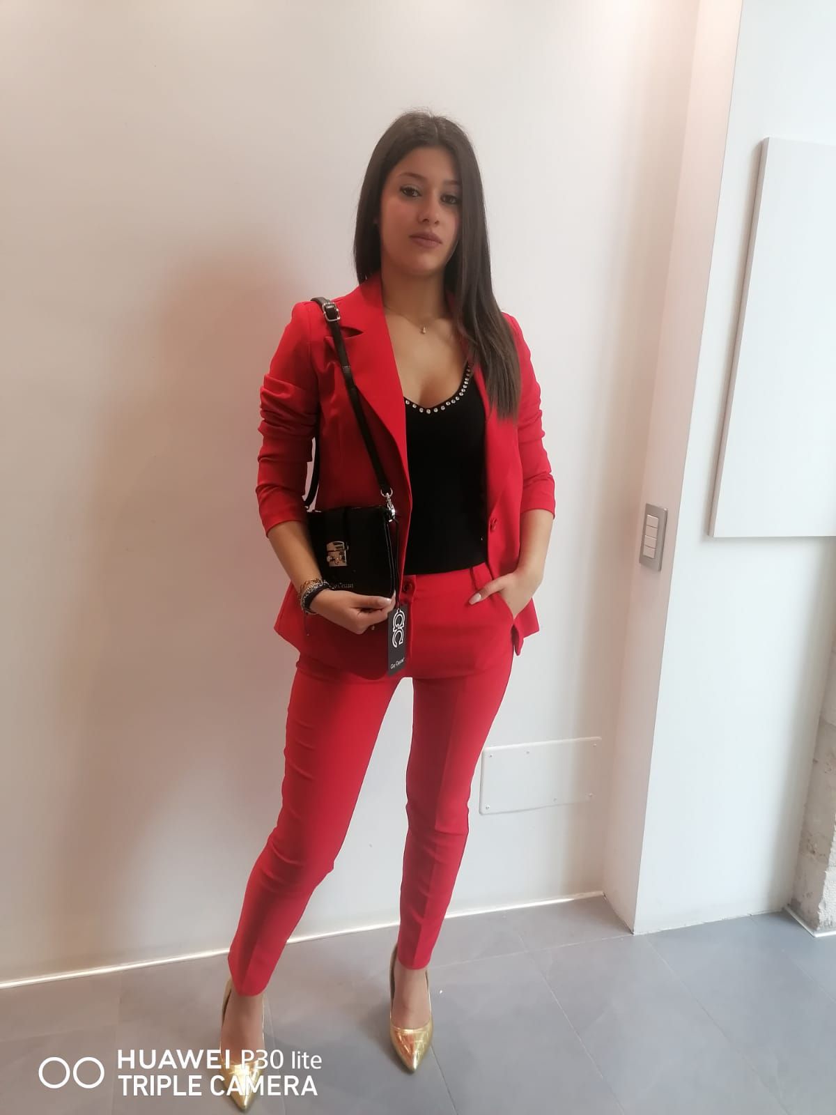 Una donna in abito rosso è in piedi davanti a un muro bianco.