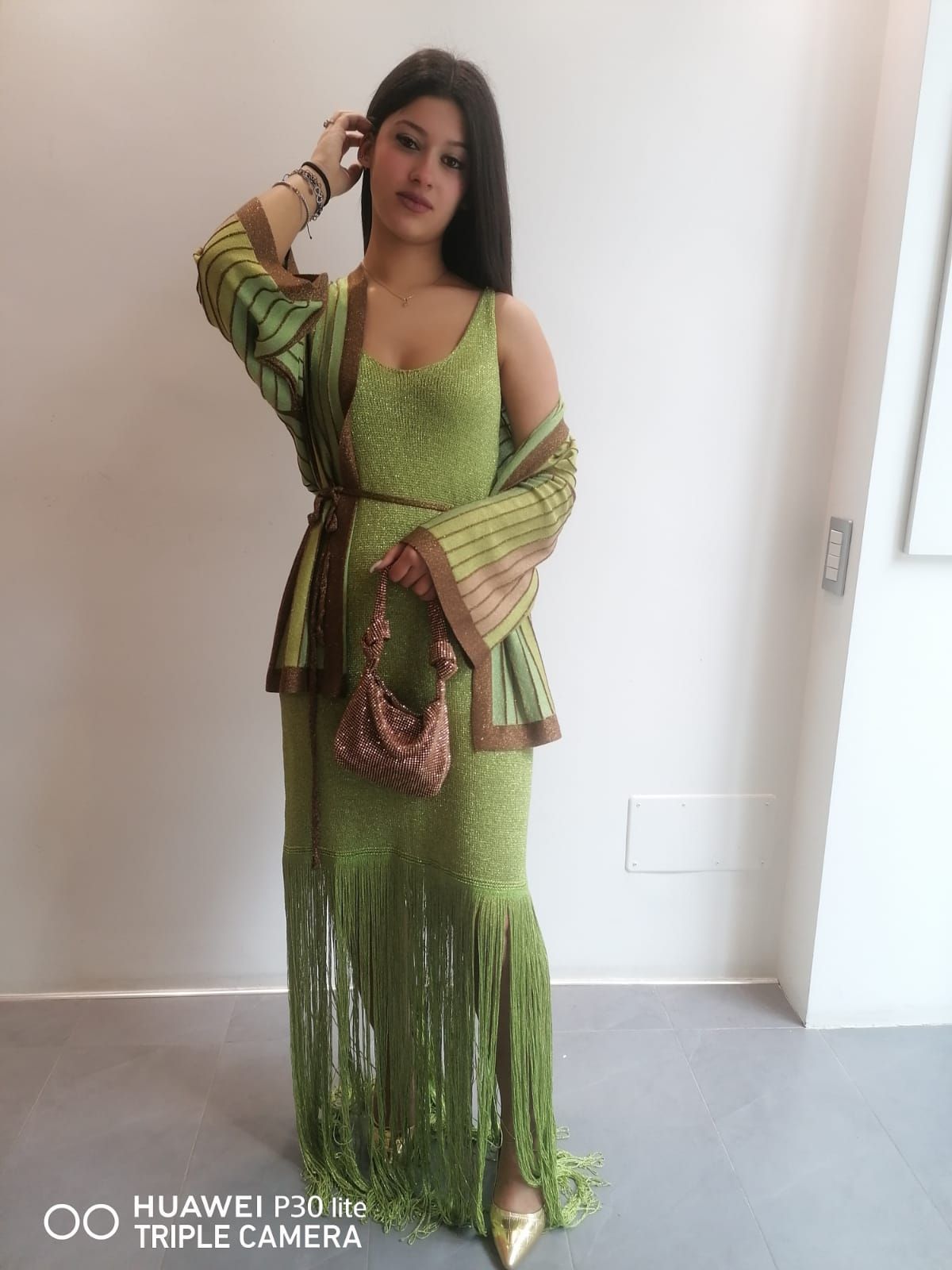 Una donna con un vestito verde è in piedi davanti a un muro bianco.