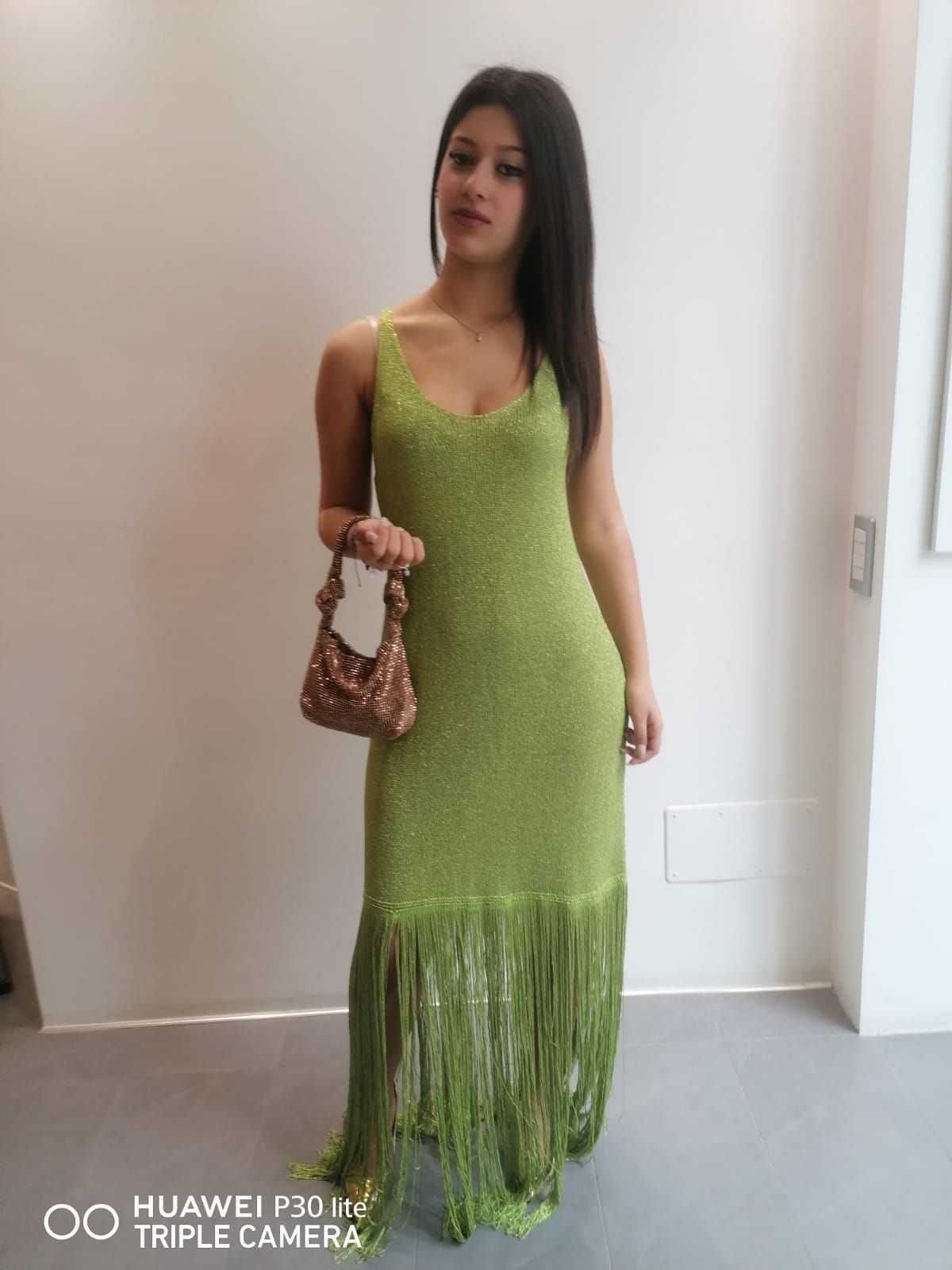 Una donna indossa un vestito verde e tiene in mano una borsa.
