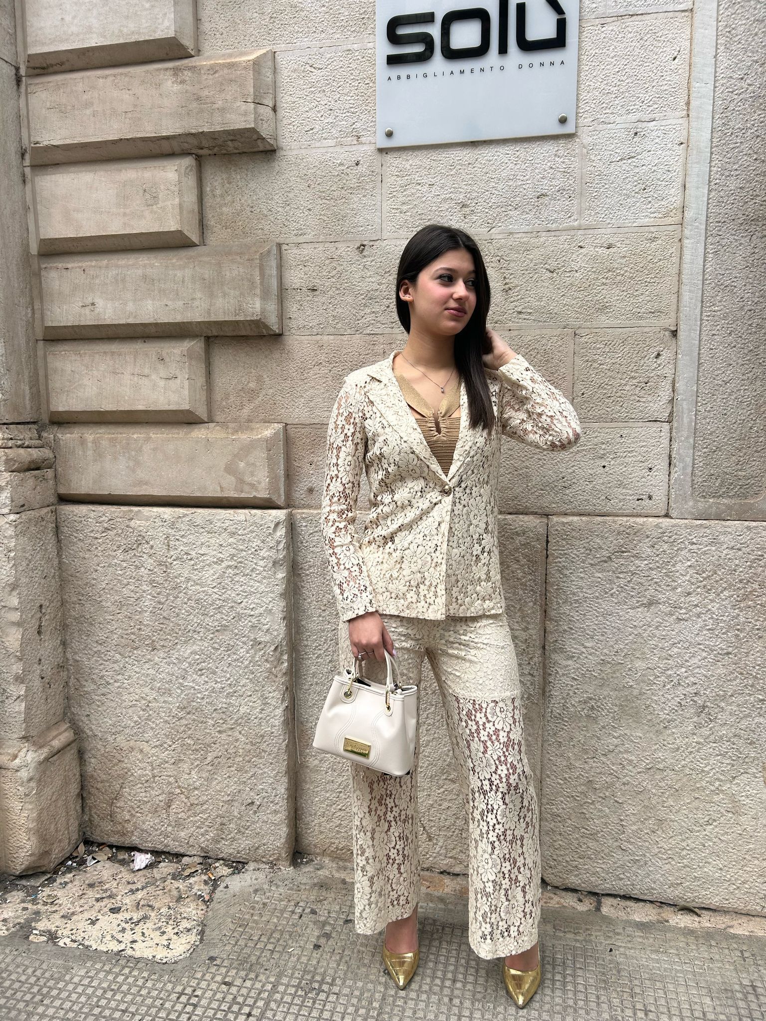 Una donna con un tailleur di pizzo bianco è in piedi davanti a un edificio.