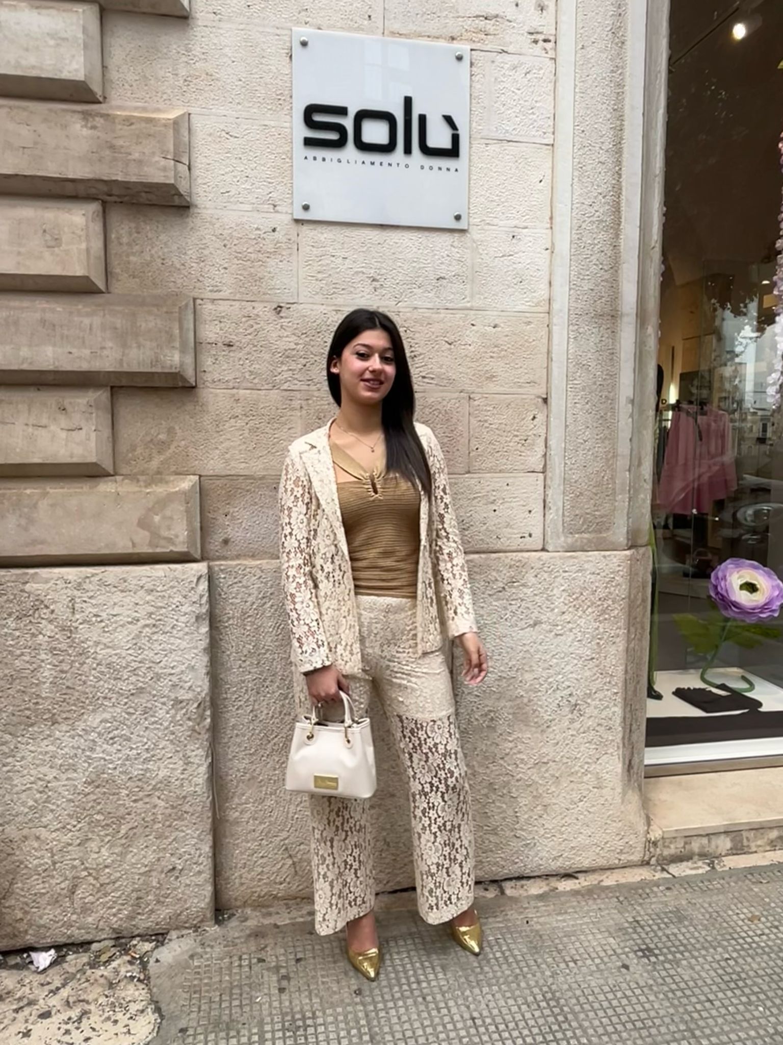 Una donna con un tailleur di pizzo è in piedi davanti a un negozio.