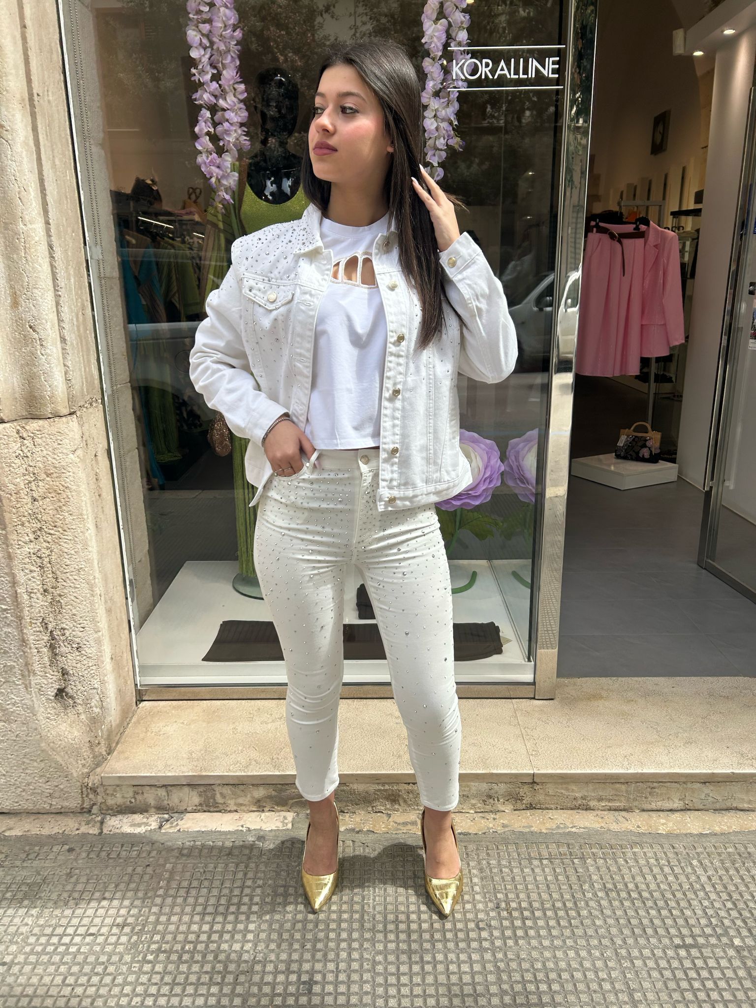 Una donna che indossa una giacca di jeans bianca e pantaloni bianchi è in piedi davanti a un negozio.
