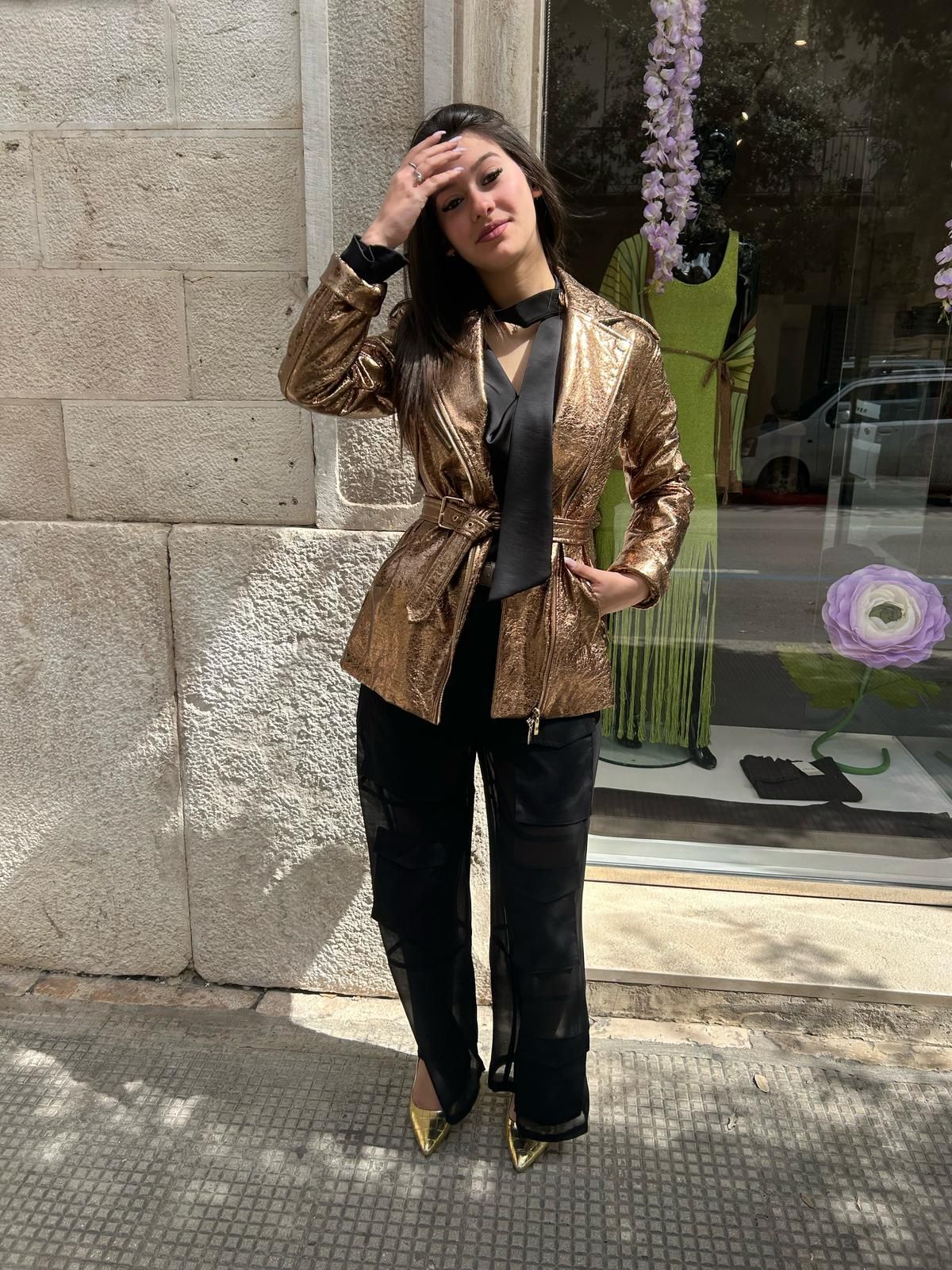 Una donna che indossa una giacca dorata e pantaloni neri è in piedi davanti alla vetrina di un negozio.