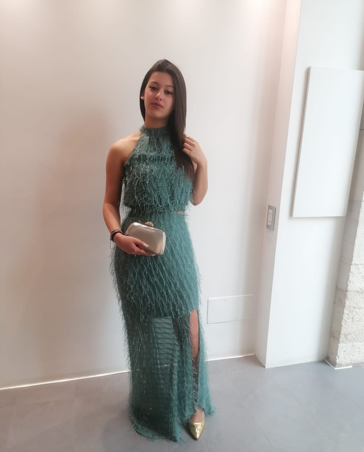 Una donna con un vestito verde è in piedi in una stanza e tiene in mano una pochette.