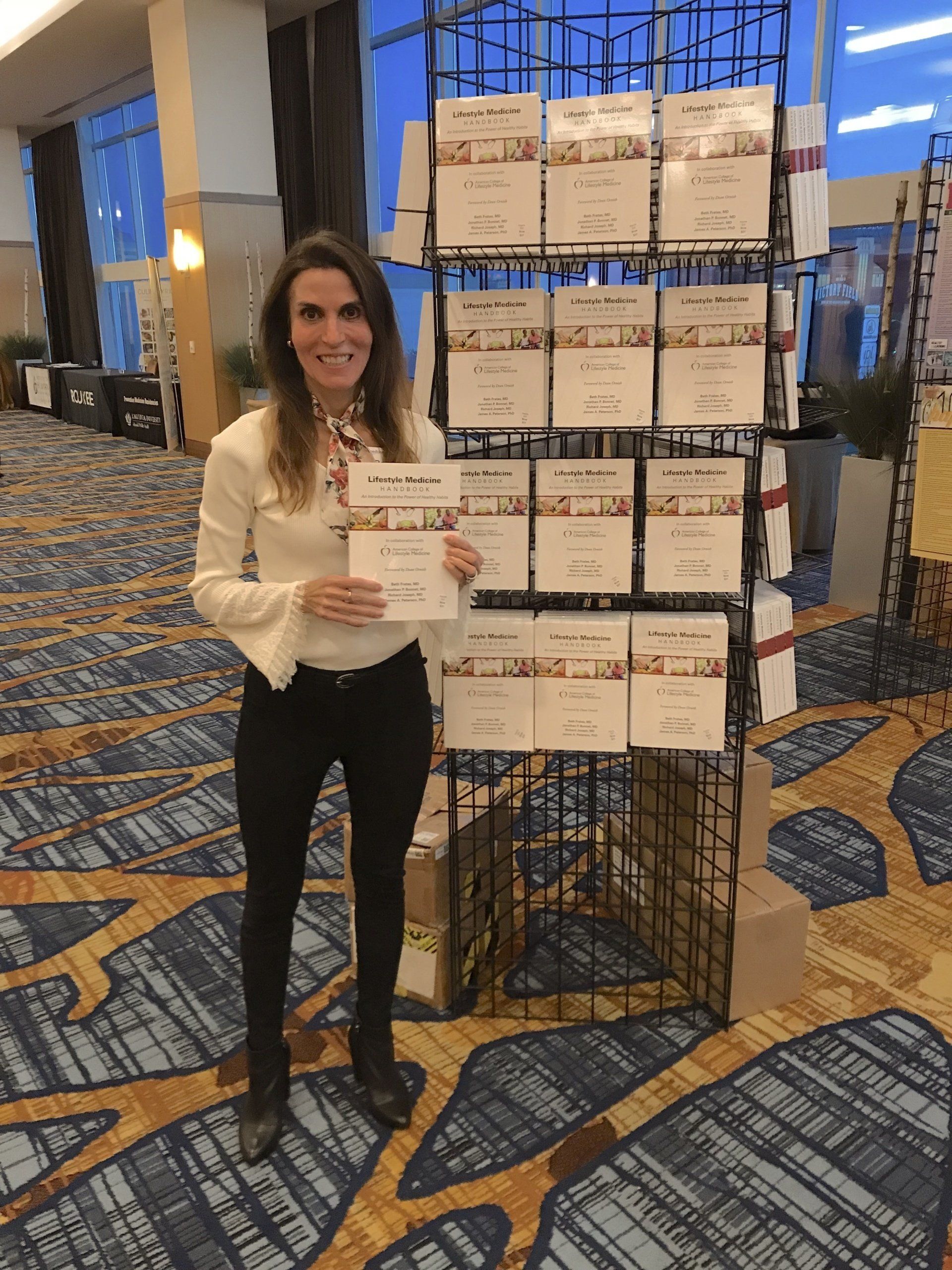 Dr. Beth Frates at the 2018 ACLM conference with copies of her book The Lifestyle Medicine Handbook: An Introduction to the Power of Healthy Habits.