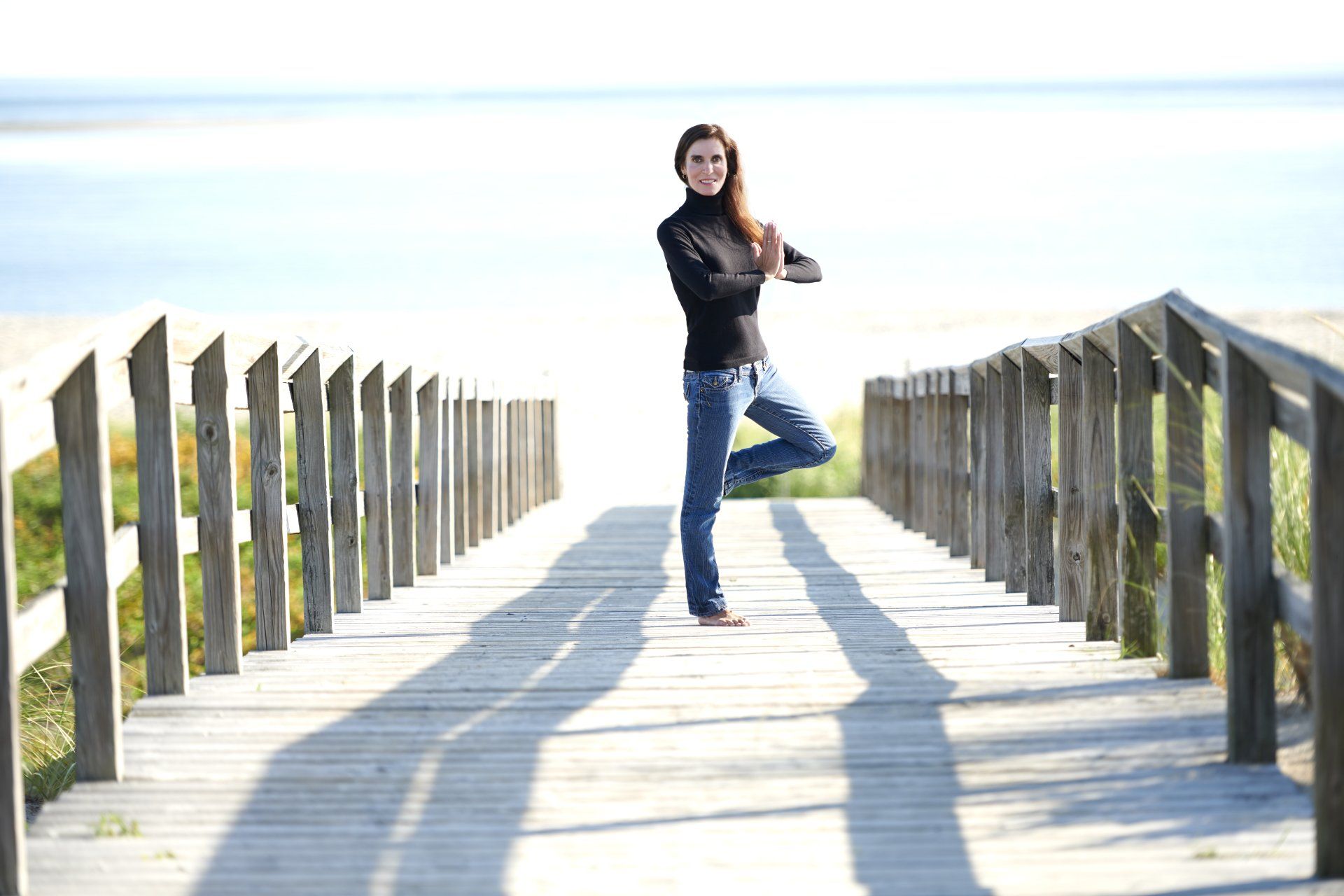 Beth Frates MD standing on one leg on a wooden boardwalk.