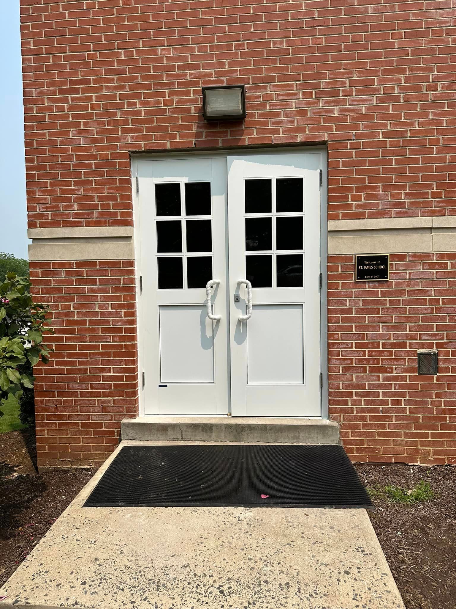 A brick building with two white doors and a black mat on the ground.