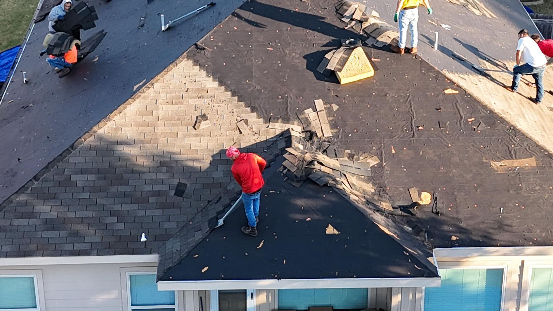 A man in a red shirt is working on the roof of a house.