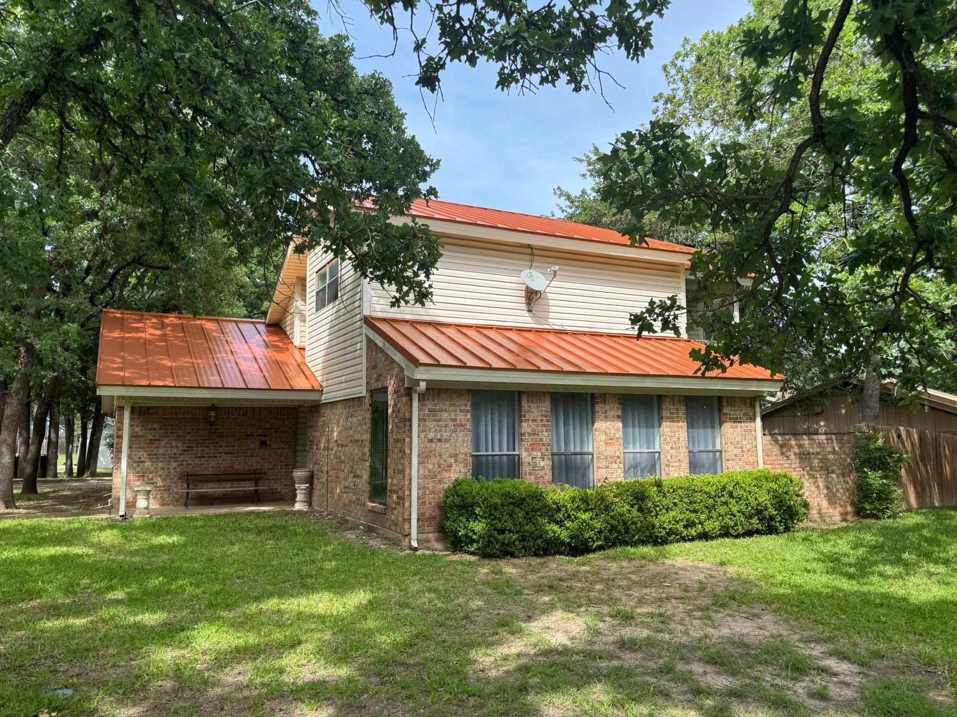A brick house with a red roof is surrounded by trees and grass.