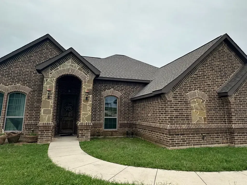 A large brick house with a gray roof and a walkway leading to it.
