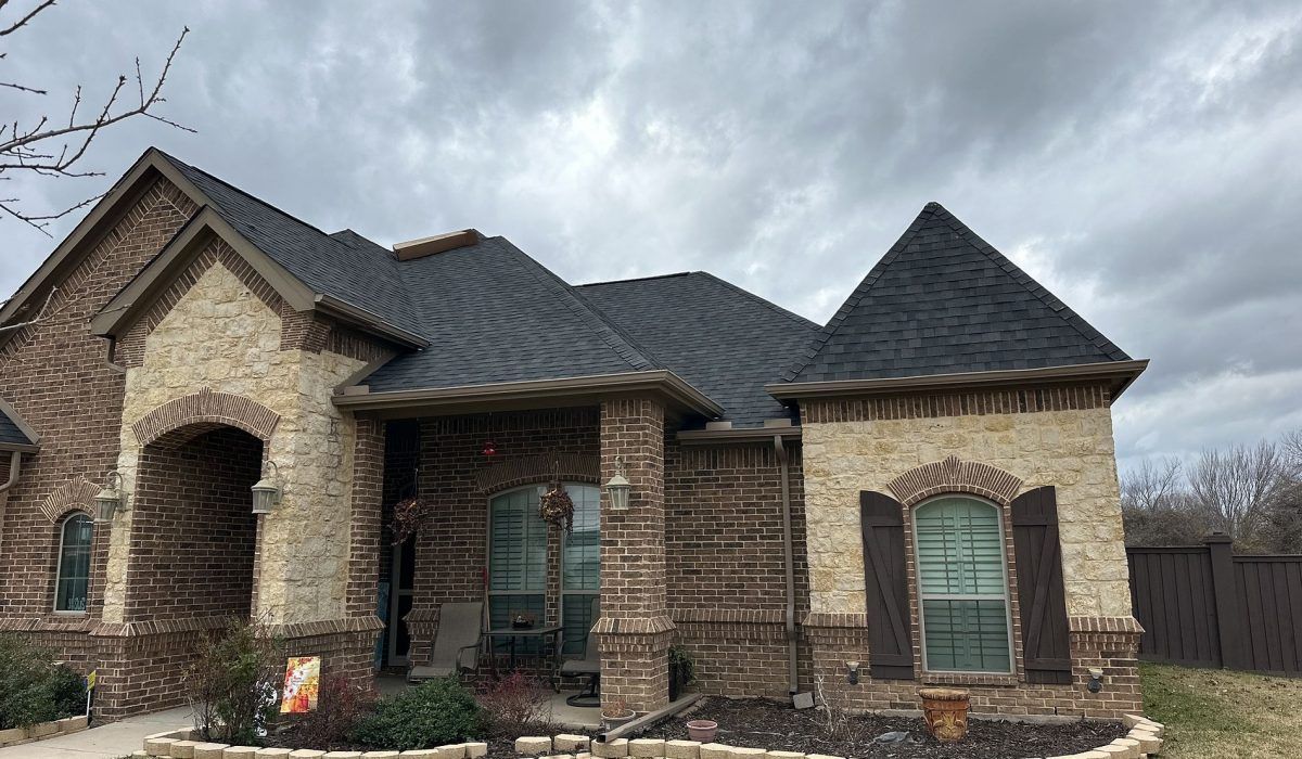 A large brick house with a black roof and shutters.